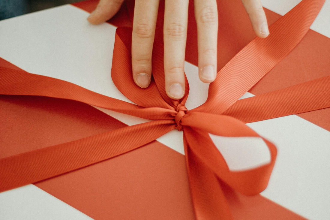 Close up of hands tying a bright red ribbon around a white gift box.