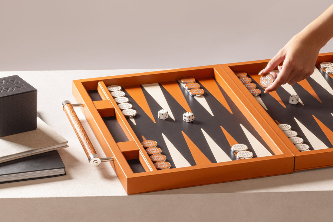 Open orange backgammon set with white and orange playing pieces and dice on a neutral surface as a hand moves a piece