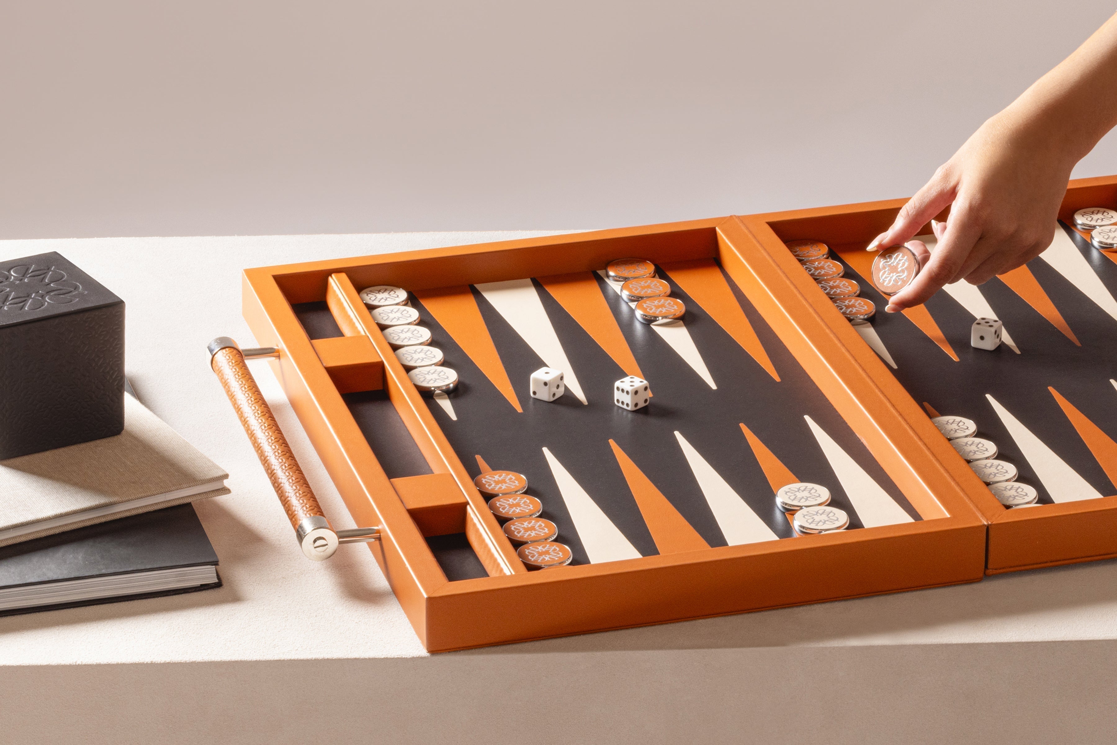 Open orange backgammon set with white and orange playing pieces and dice on a neutral surface as a hand moves a piece