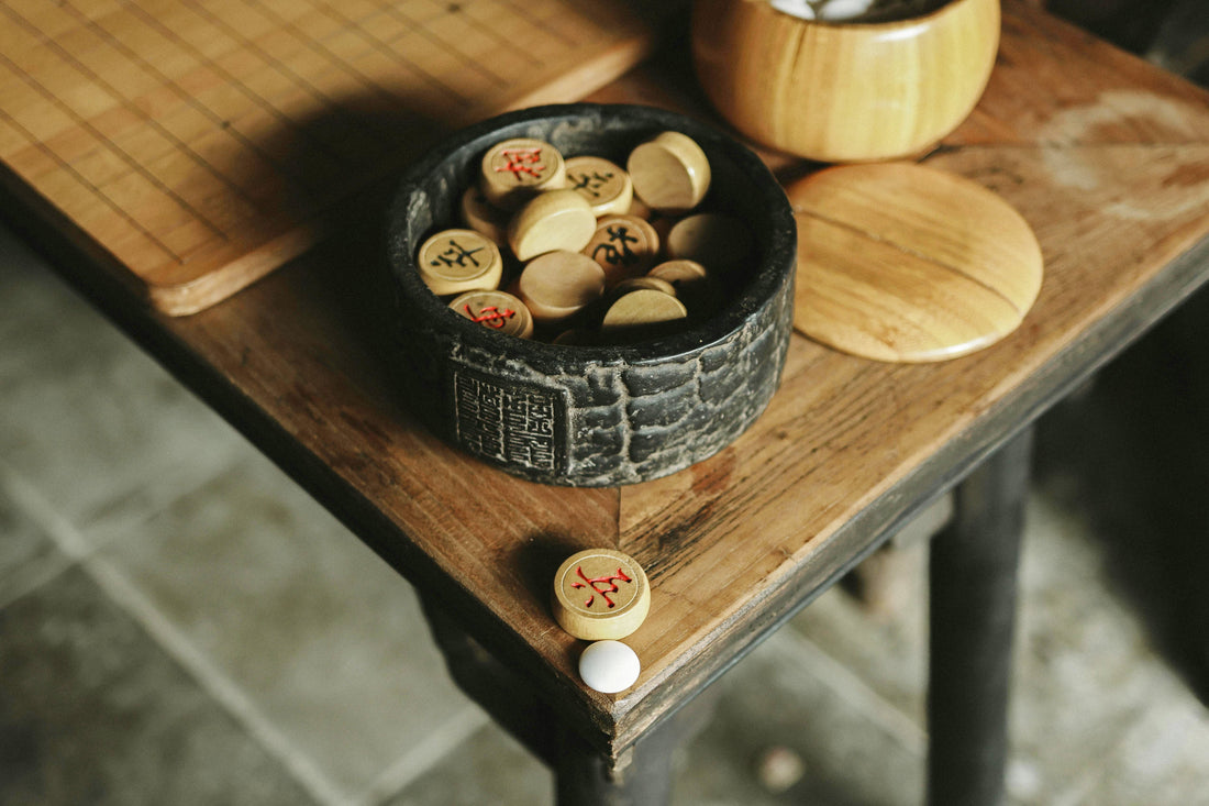 Xiangqi chess pieces inside a round black container on a wooden table with a few pieces spilled nearby