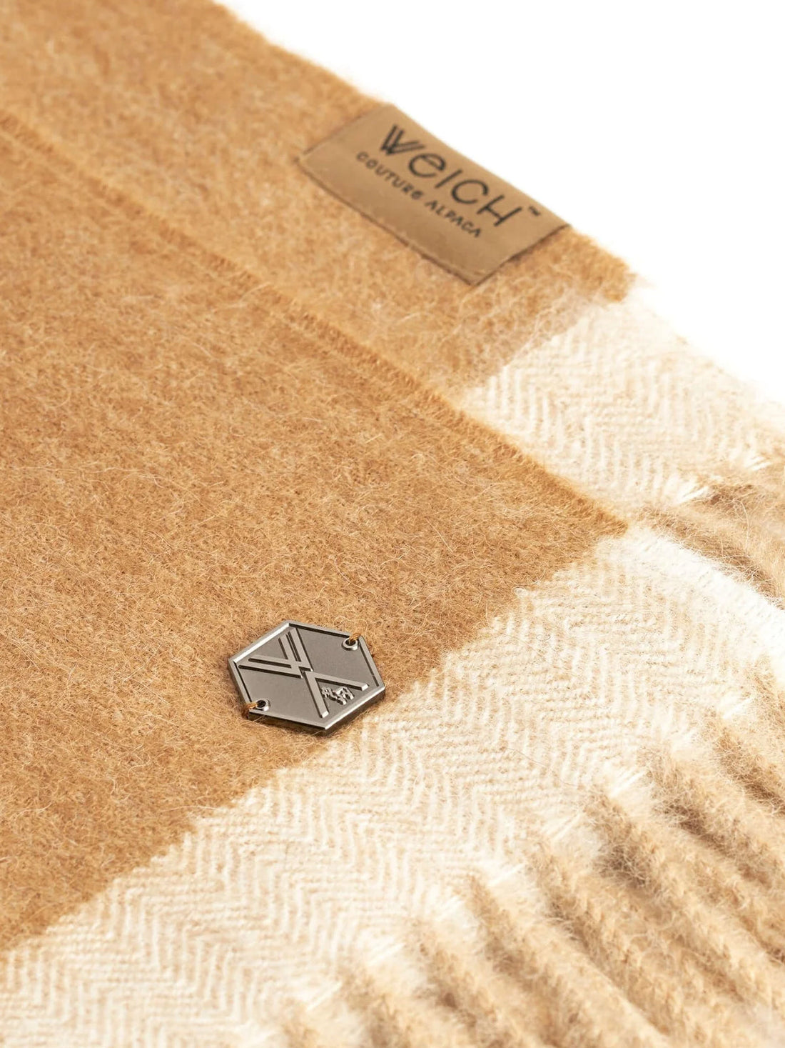 Close up of a fuzzy beige and cream textile with a small hexagonal metal tag.