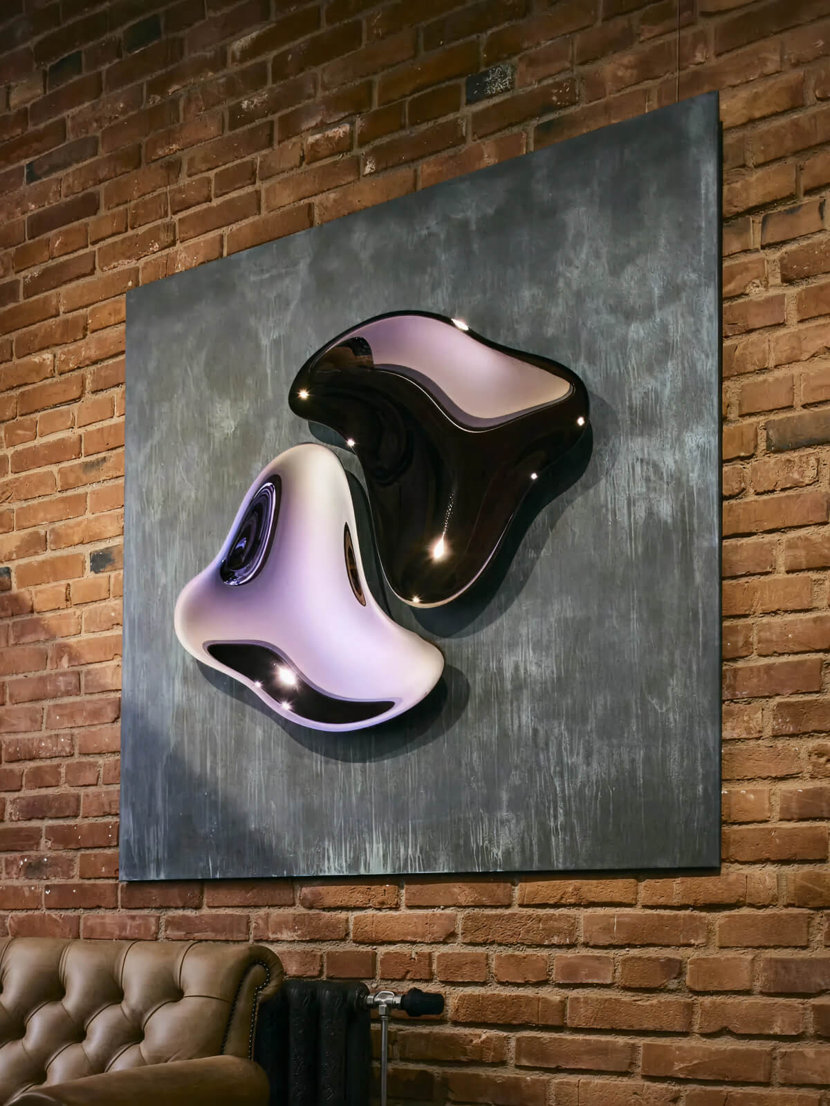 Large contemporary glossy sculpture in lavender and black mounted on a textured blue panel against a brick wall