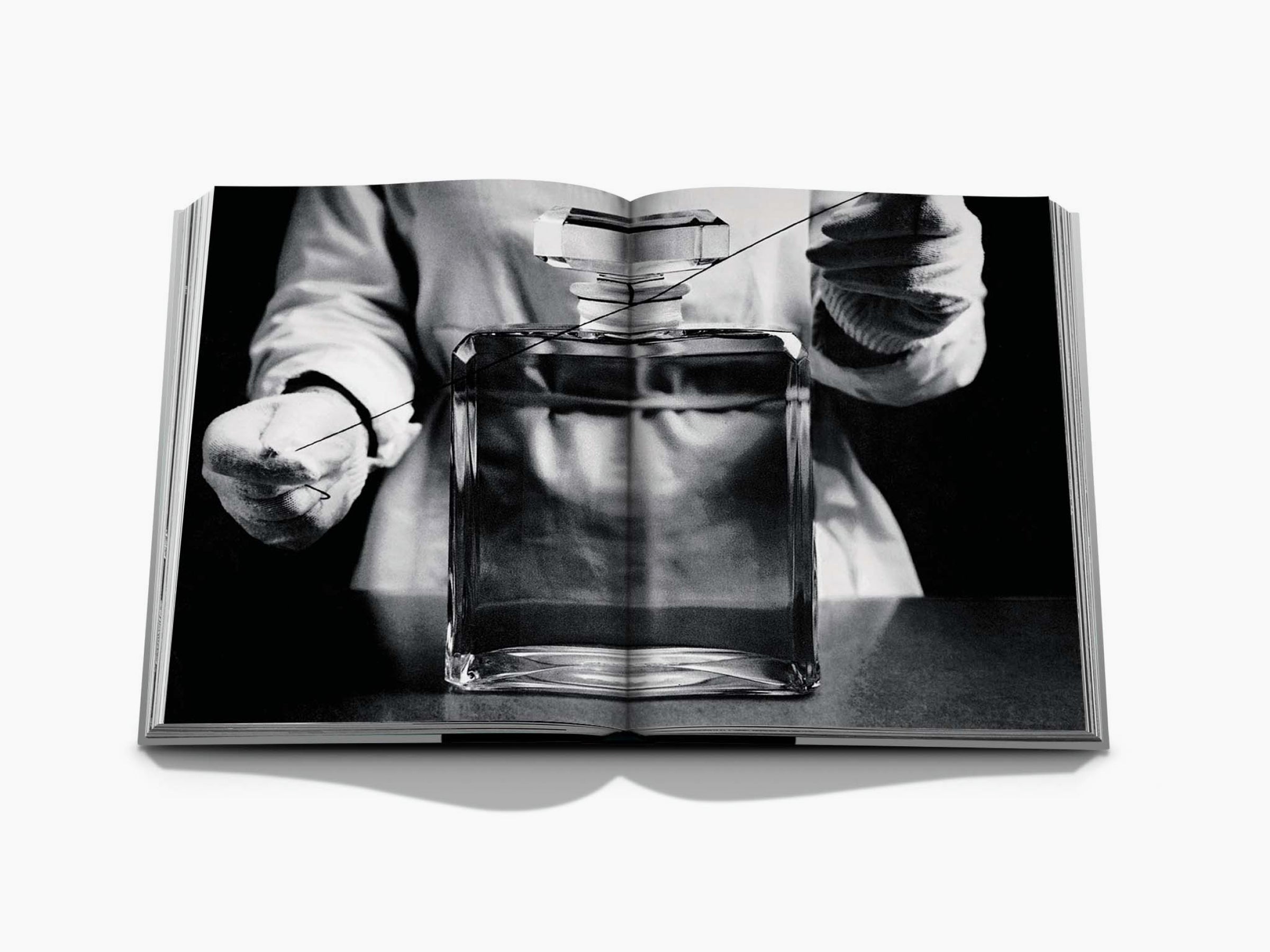 Monochrome studio shot of a perfume bottle being handled by gloved hands with a threading line around it