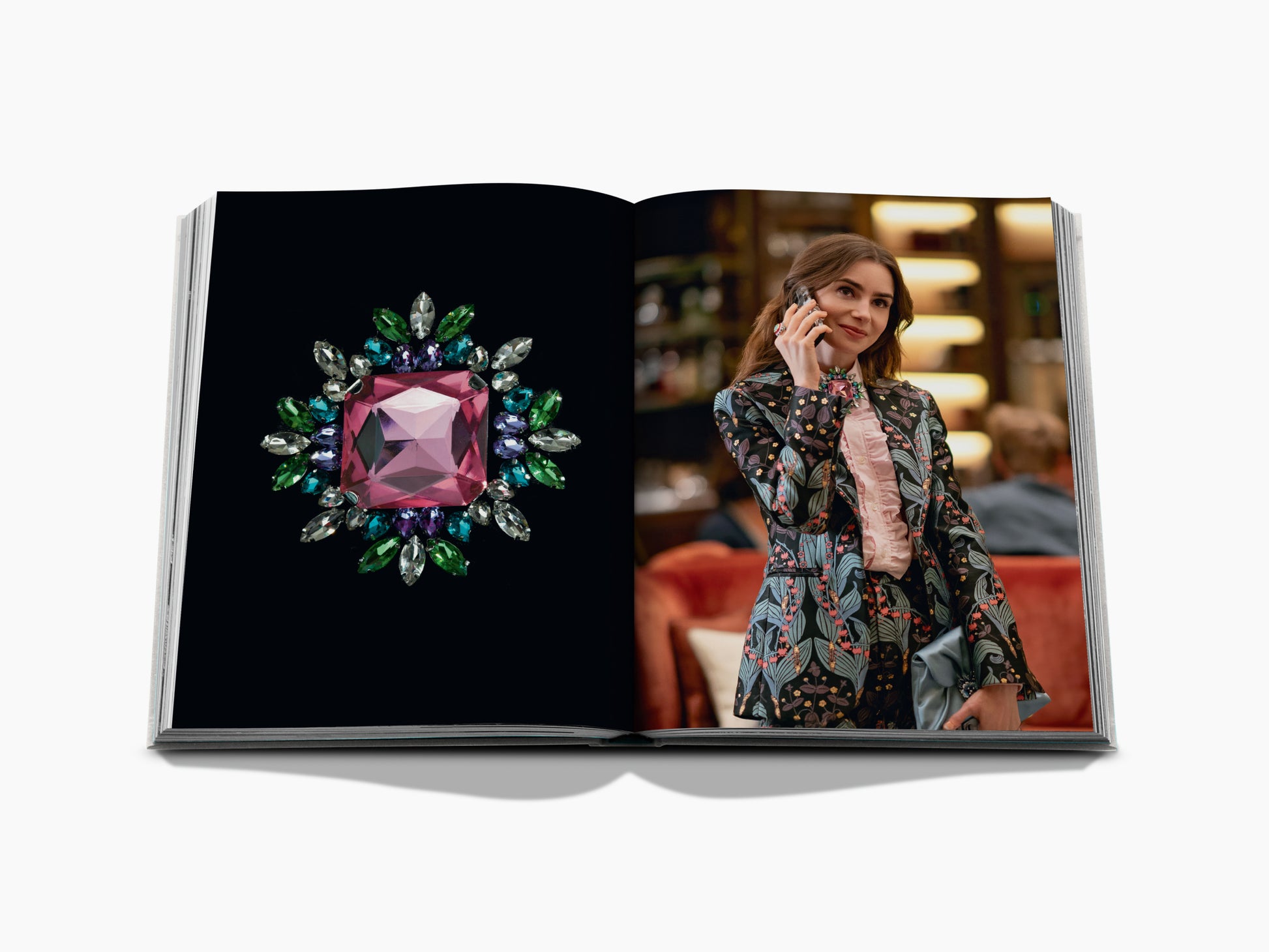 Open fashion book spread showing a jeweled pink square brooch on the left page and a woman in a floral suit on the right.