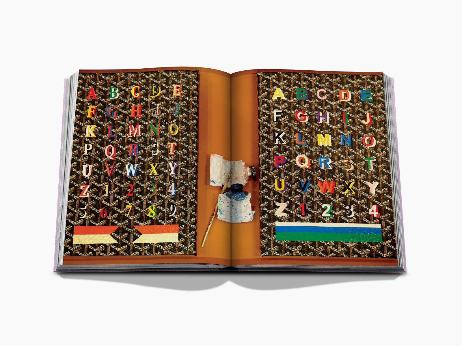 Open book spread with a brown geometric pattern, colorful alphabet letters across both pages, and an orange central spine with art supplies