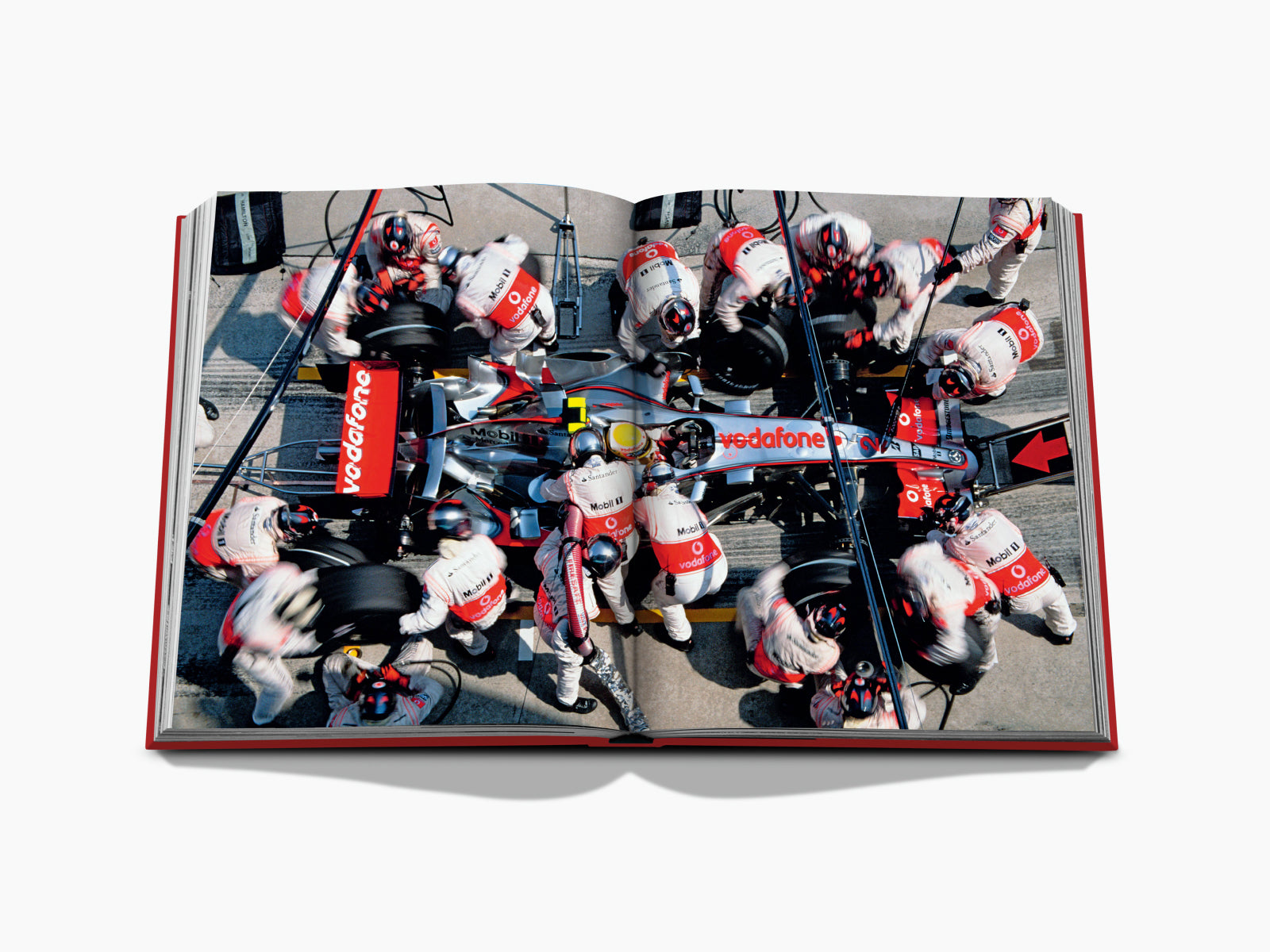 Overhead view of a Vodafone Formula 1 car amid pit crew, spread across a two-page opening in Formula 1 The Impossible Collection