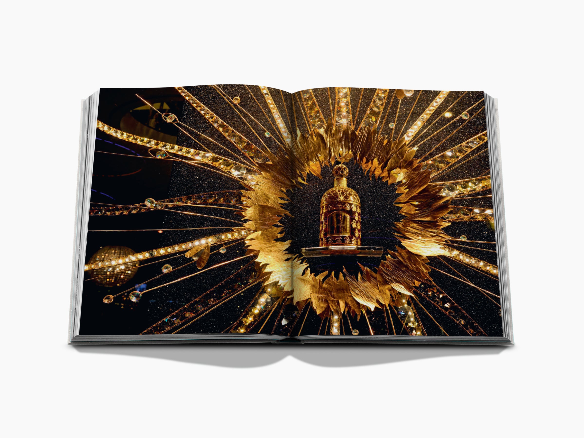 Open Guerlain book spread featuring a lavish gold sunburst surrounding a perfume bottle against a dark background.