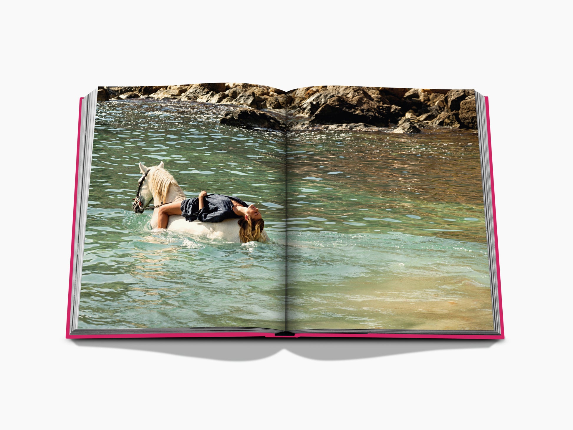 Open book spread showing a person reclining on a white horse in turquoise water near a rocky shore.