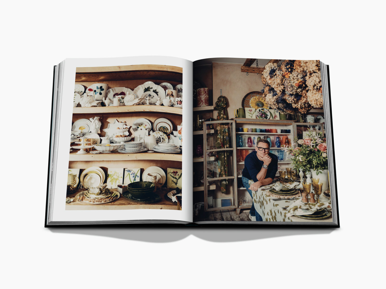 Two page spread showing shelves of ceramics on the left and a man at a dining table amid glassware and dried flowers on the right.