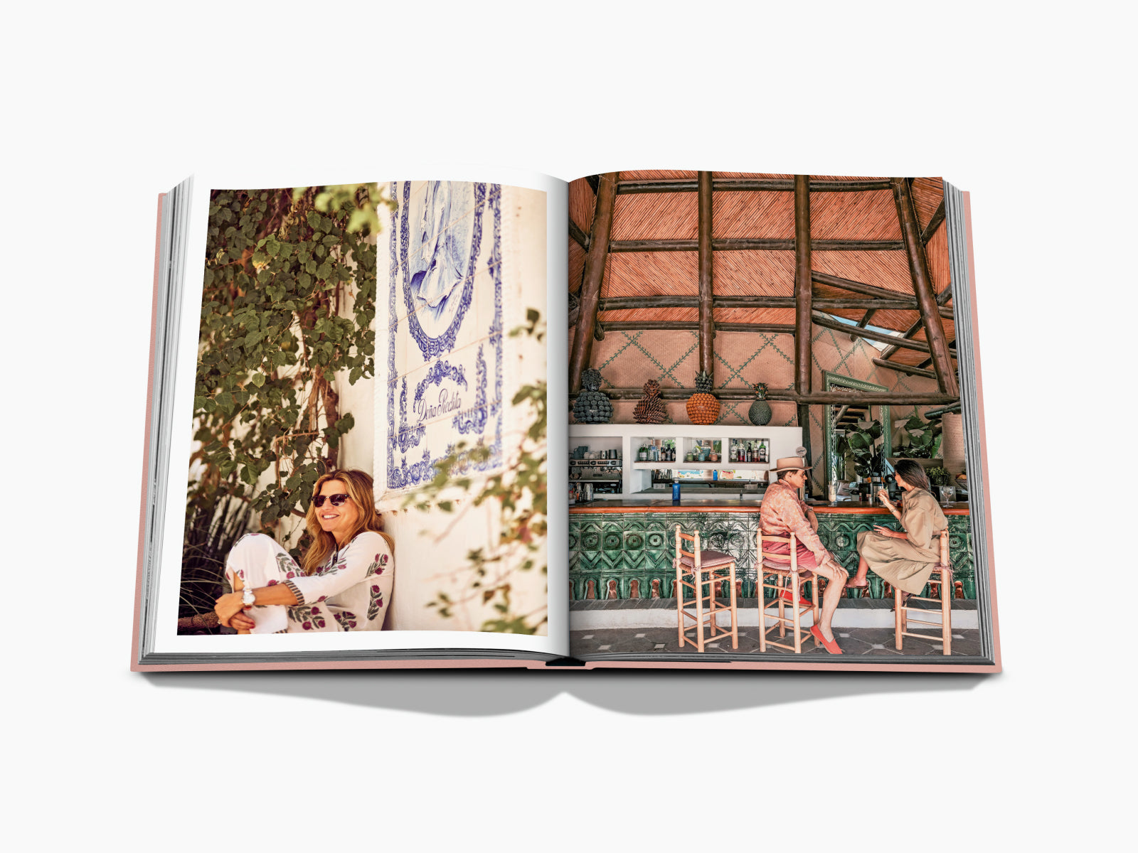 Woman in sunglasses sits on a sunlit balcony against a white wall with a blue ceramic mural and lush greenery.