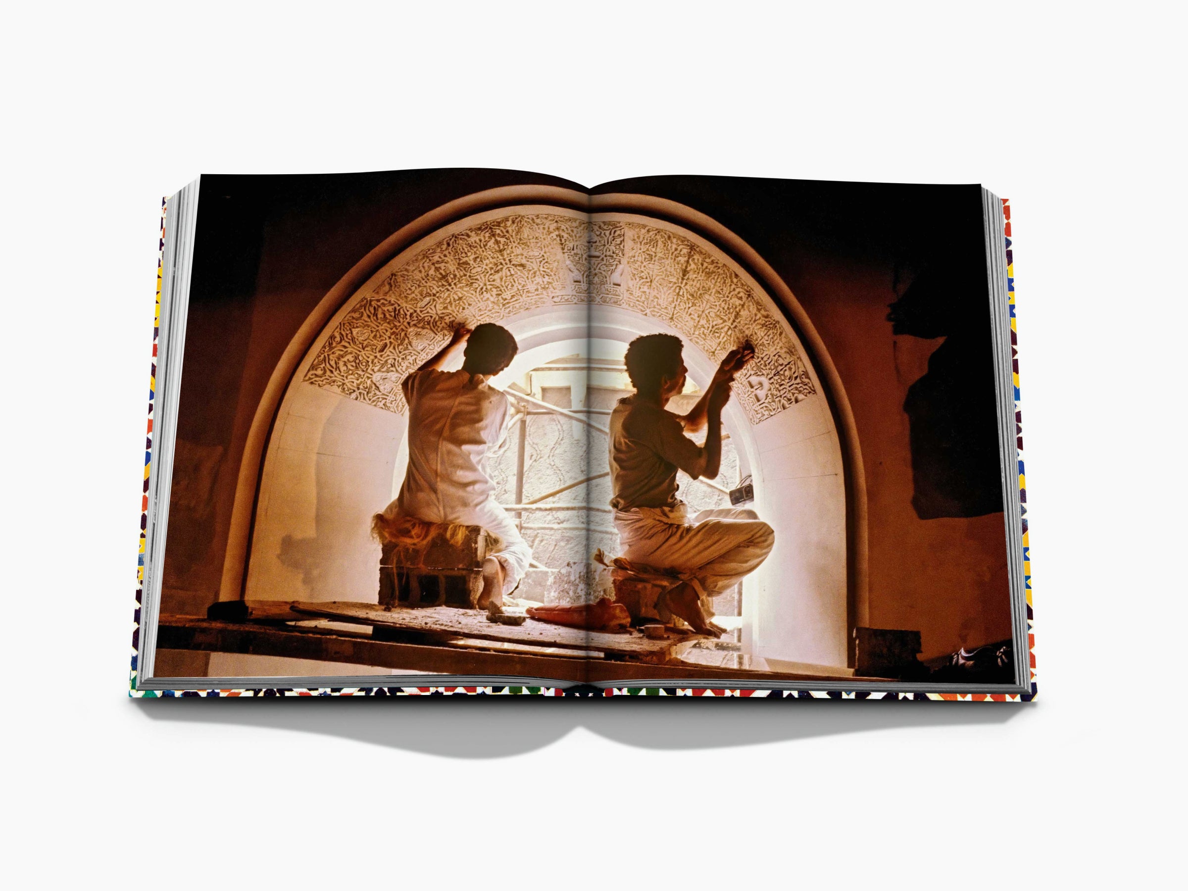 Open book spread showing two artisans kneeling inside a warmly lit ornate arched doorway.