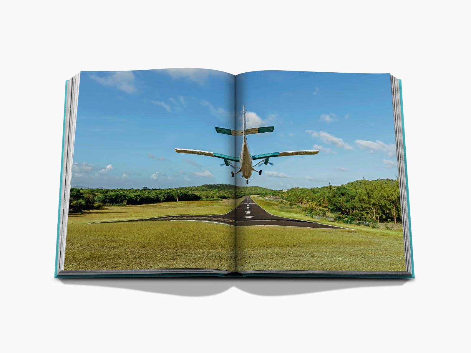 Small propeller plane landing on a tropical runway surrounded by green fields and palm trees under a bright blue sky