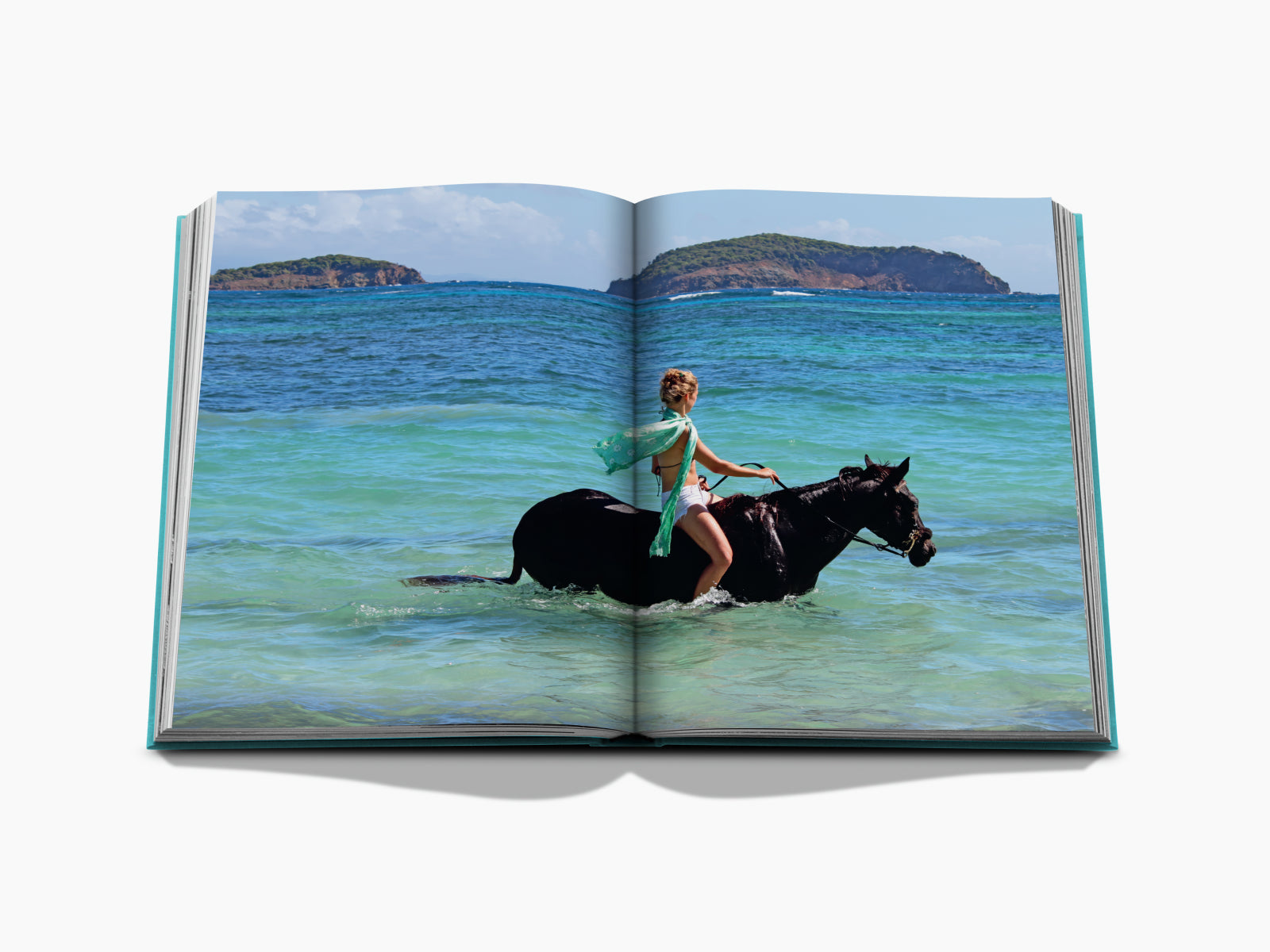 A rider on a horse wades through shallow turquoise water along a tropical beach with palm trees and distant islands