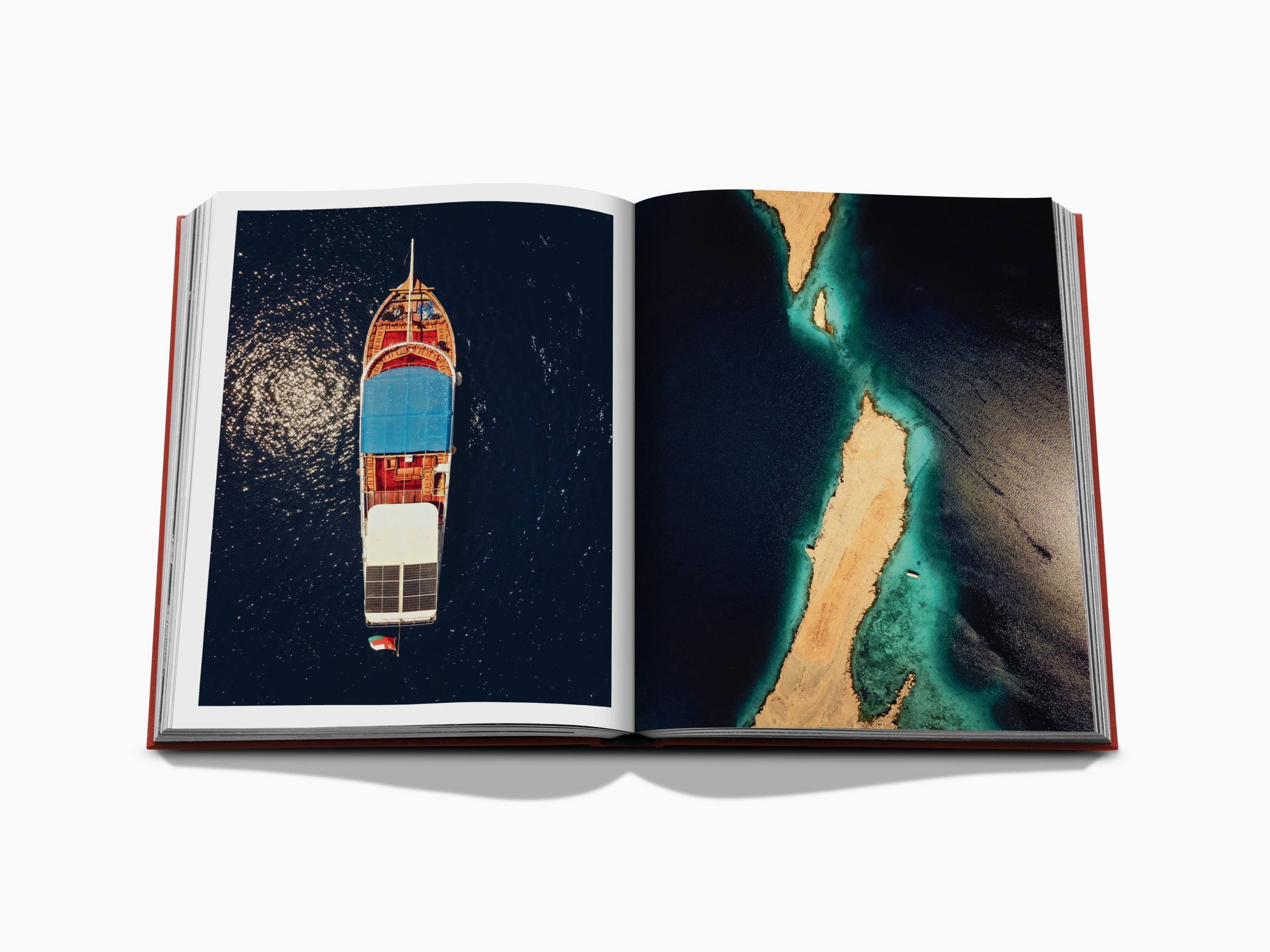Aerial view of a colorful boat on deep blue water on the left page, and turquoise sea with sandy landforms on the right page.