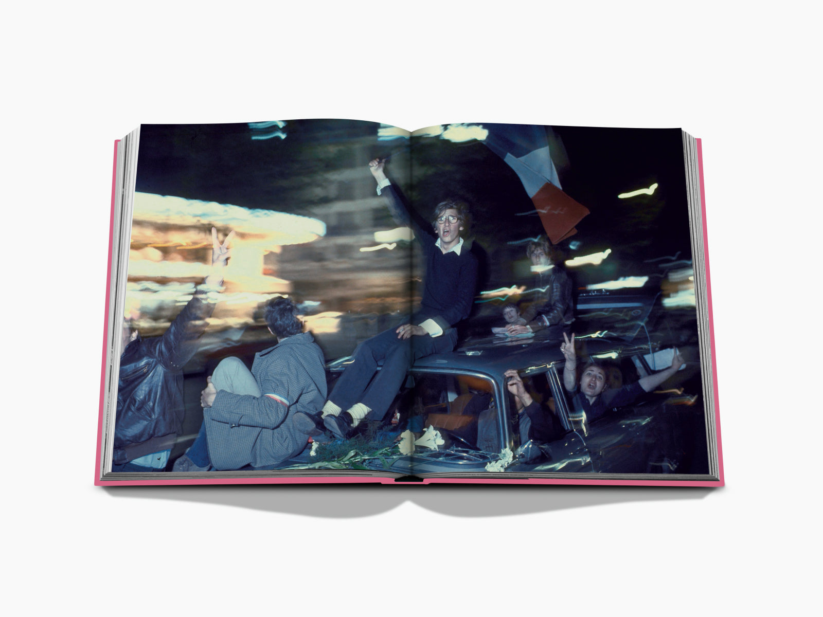 Open Paris by Paris spread showing revelers perched on a car roof during a night celebration with blurred city lights.