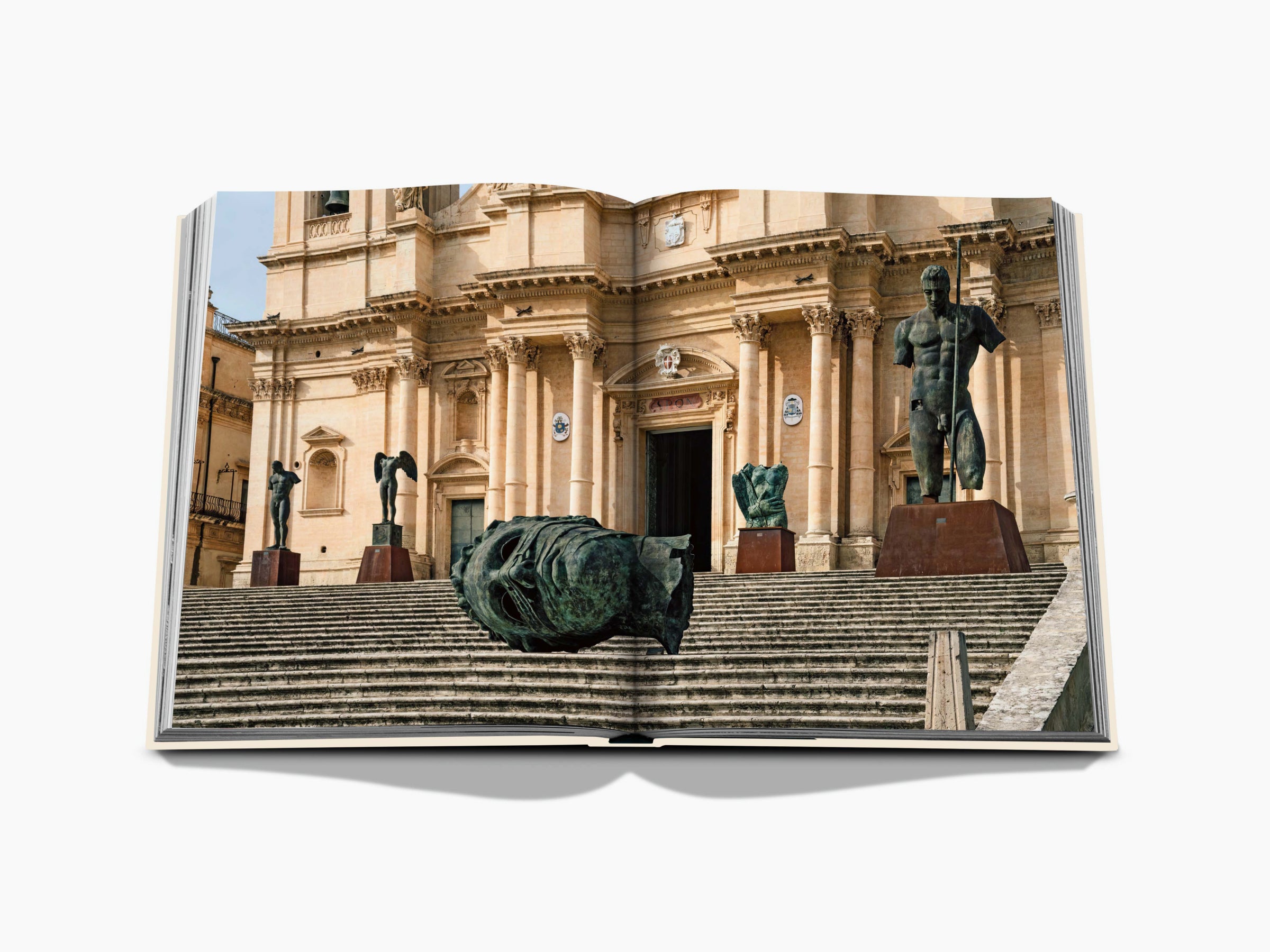 Front view of a Sicilian grand Baroque building with stairs and statues, a toppled bronze sculpture on the steps.