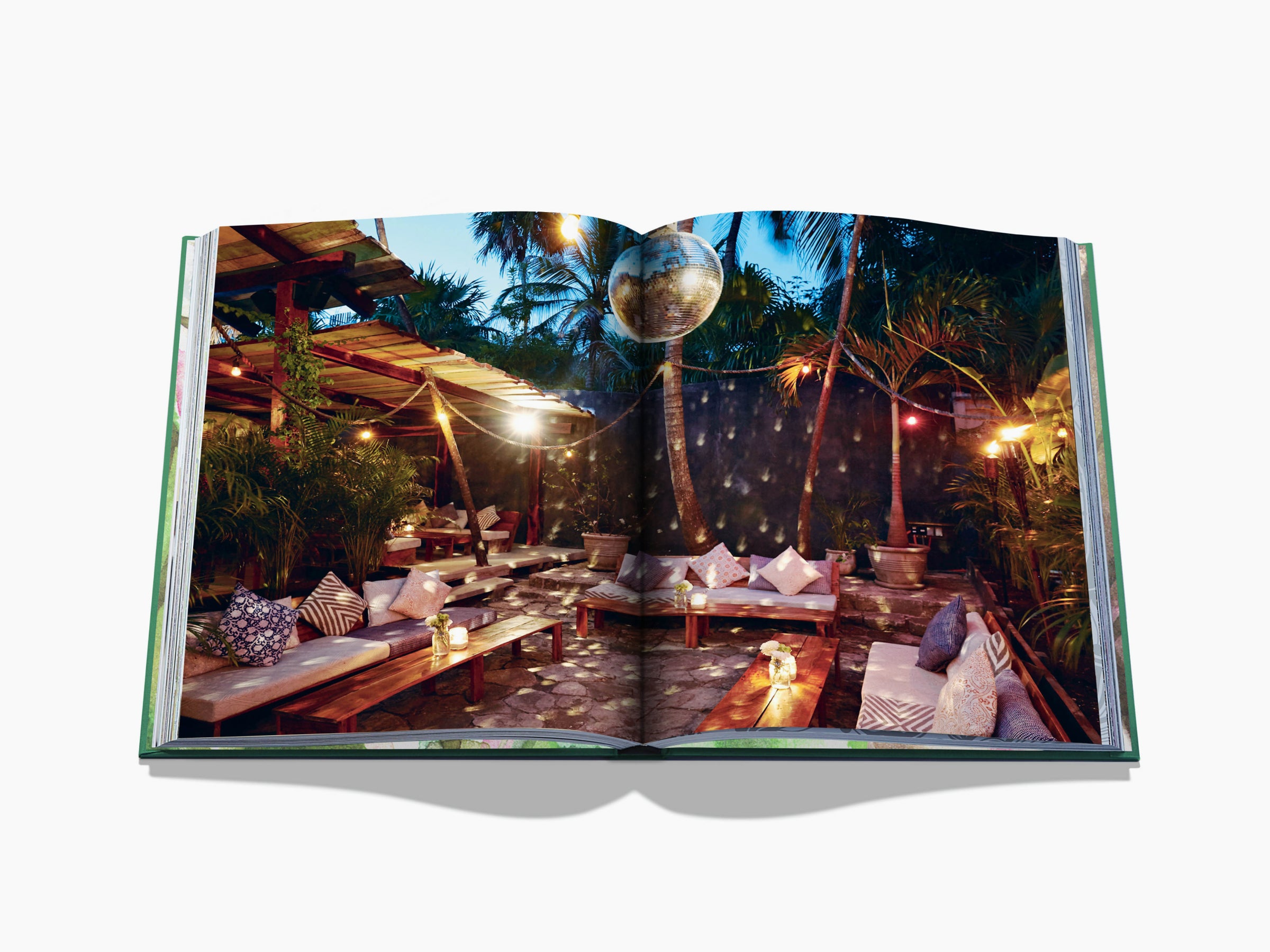 Open travel book spread of a tropical outdoor lounge with couches, cushions, string lights, and palm trees.