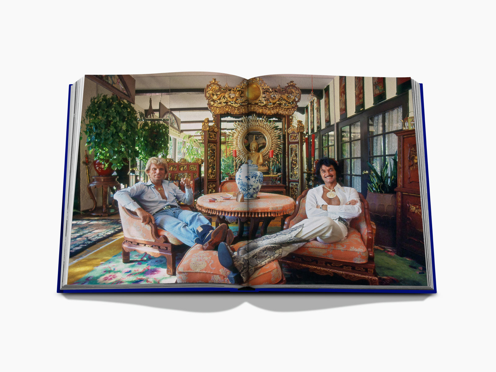 Two men lounge on ornate furniture in a lavish room with a gilded throne and a large blue and white vase.