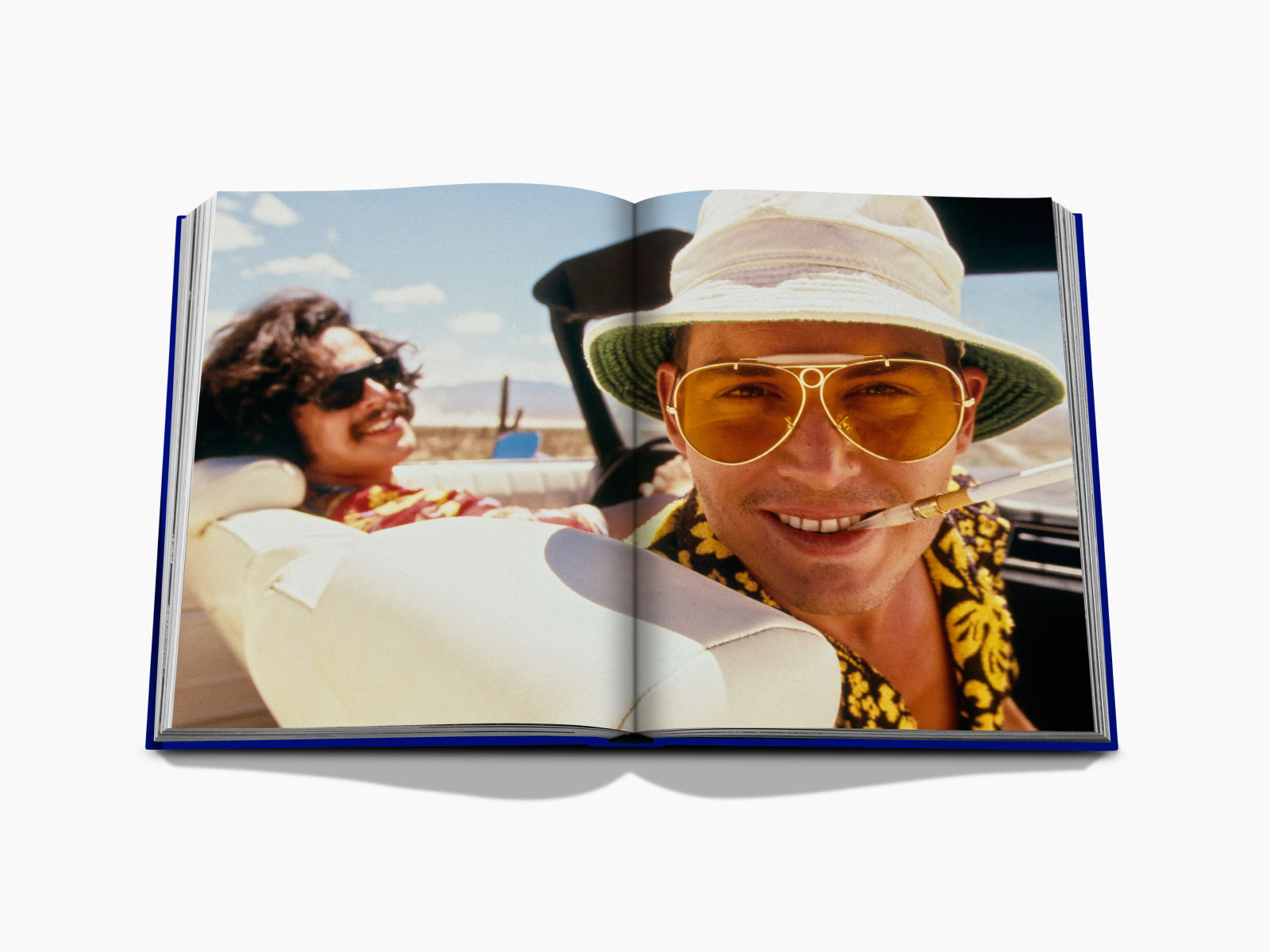 Two friends in a retro convertible driving through the desert, one wearing a bucket hat and oversized yellow aviator sunglasses.