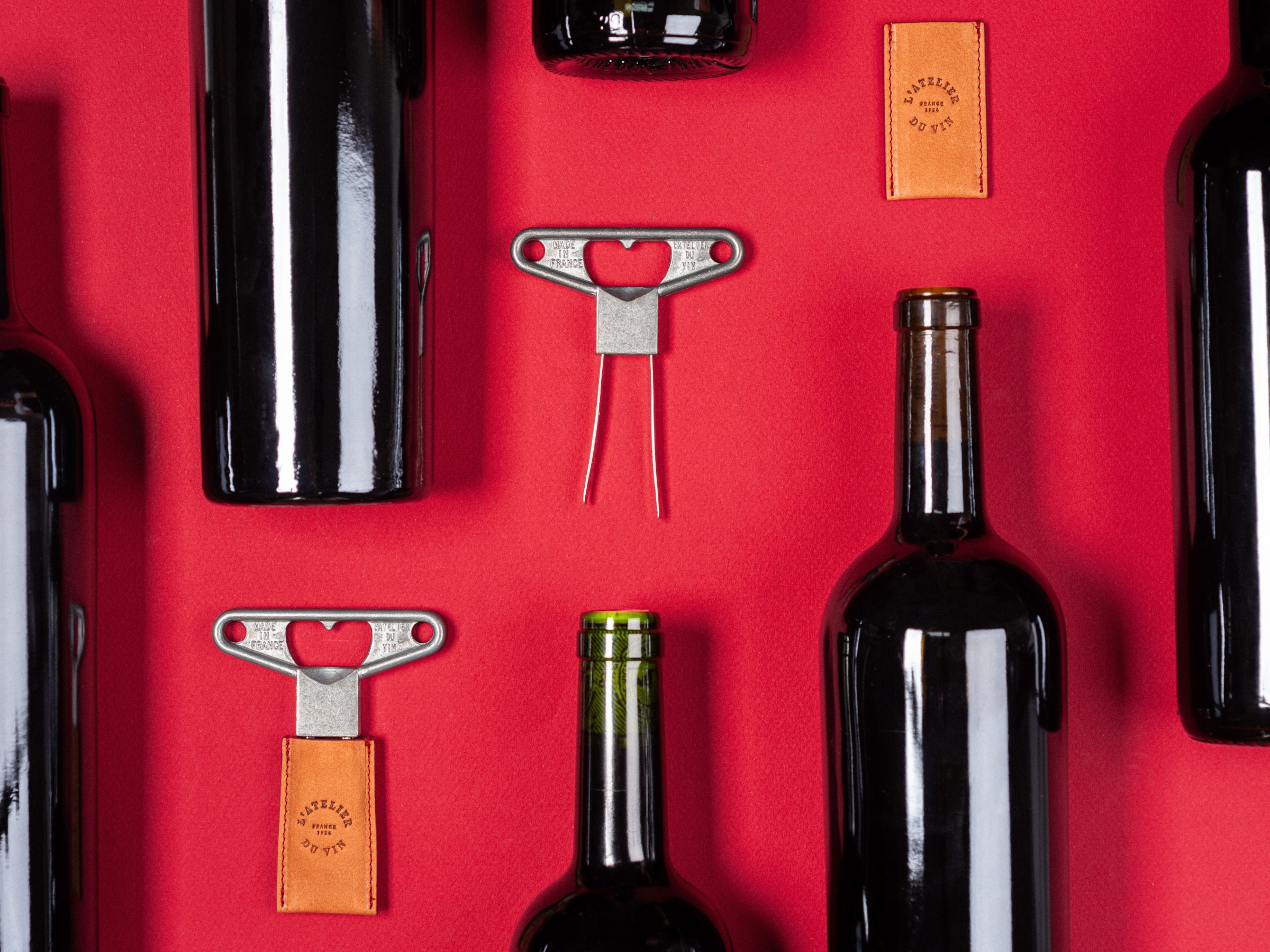 Bilame Craft twin blade corkscrew with a leather tag rests among wine bottles on a red background