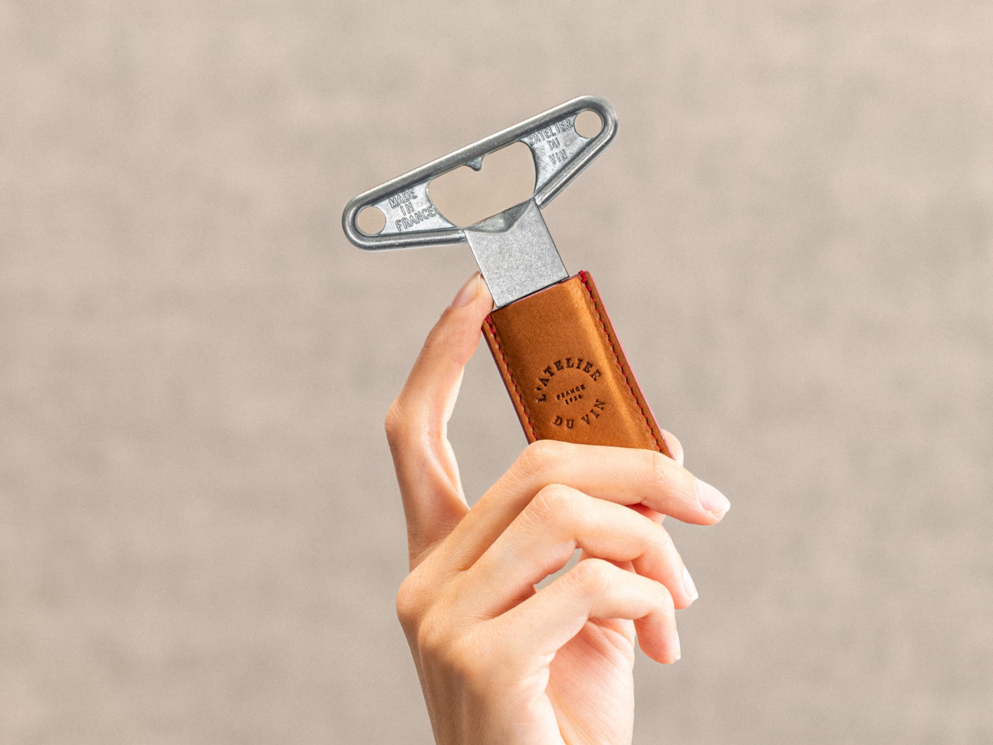 Hand holds Bilame Craft corkscrew with metal lever and leather wrapped grip against a neutral beige background