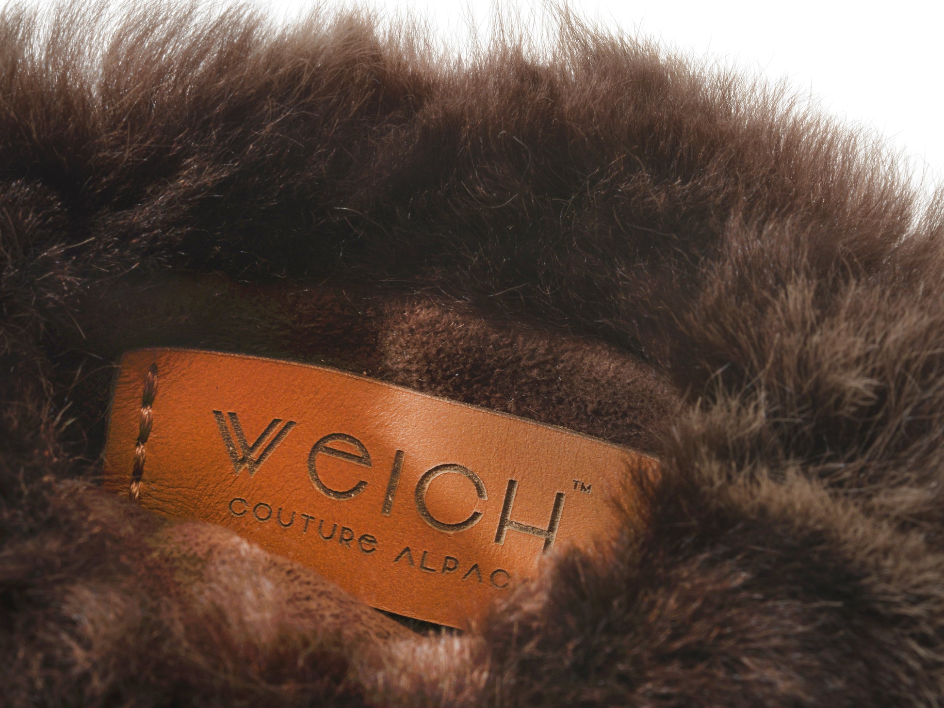 Close up of brown plush fur with tan leather label reading WEICH COUTURE ALPACA