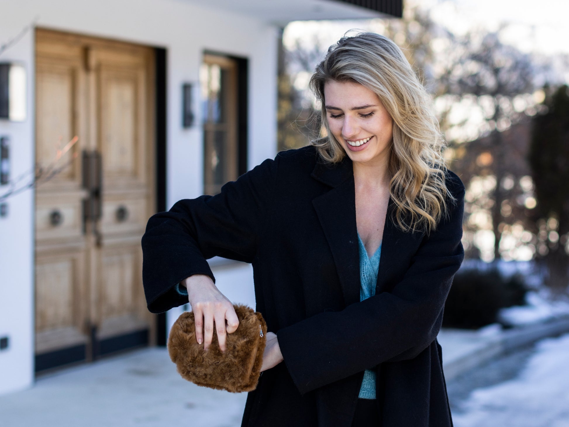 Smiling woman in a black coat holds a small brown fluffy hot water bottle wrapped in alpaca fiber.
