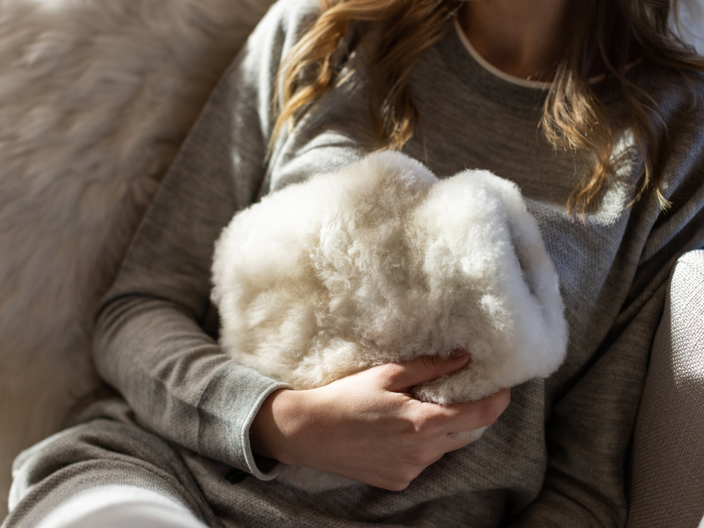 Person in a grey sweater cradling a large white alpaca fiber hot-water bottle cover