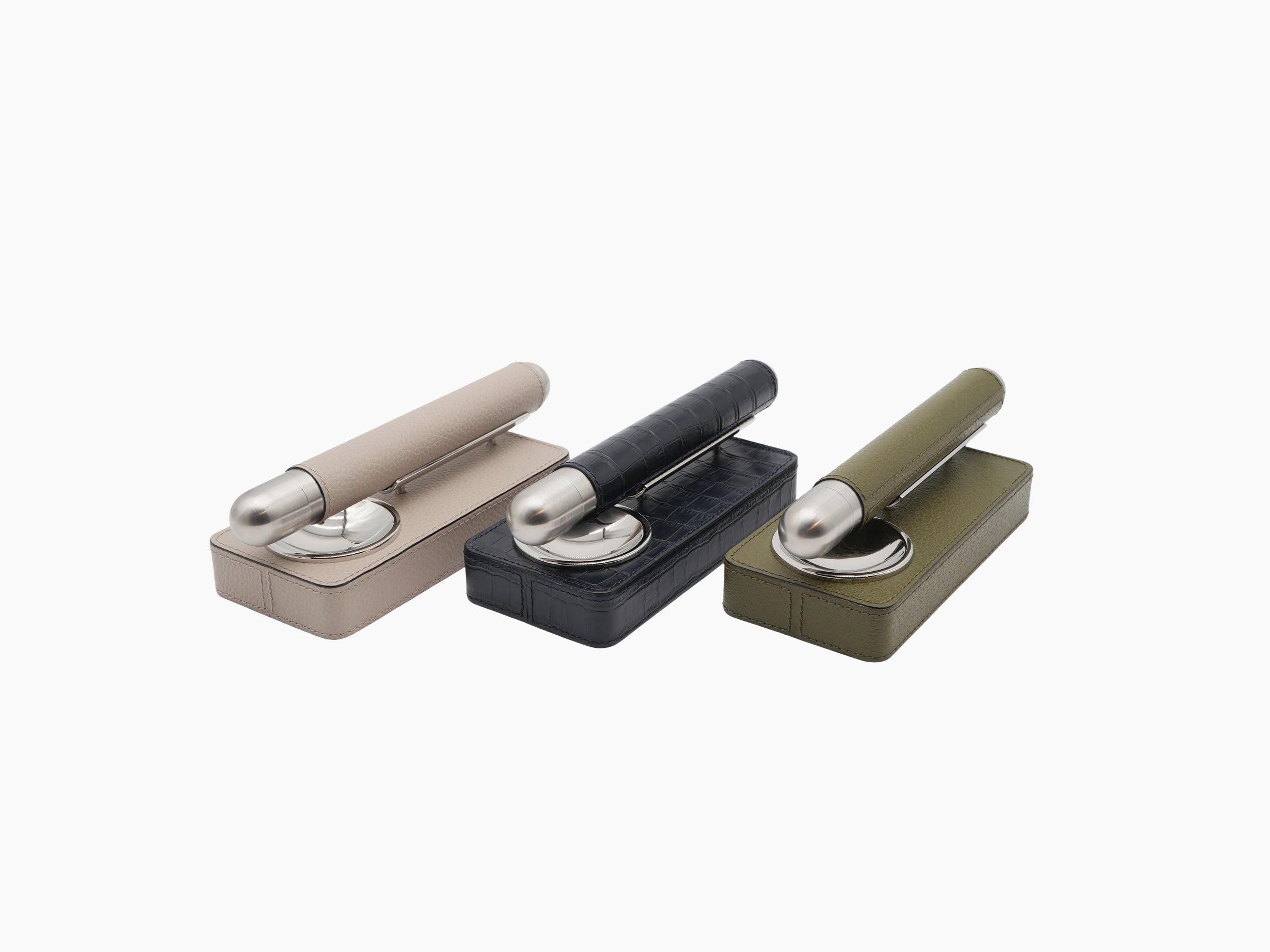 Row of three leather cigar holder sets beige navy and olive with chrome ashtrays and cigars resting on top of each case