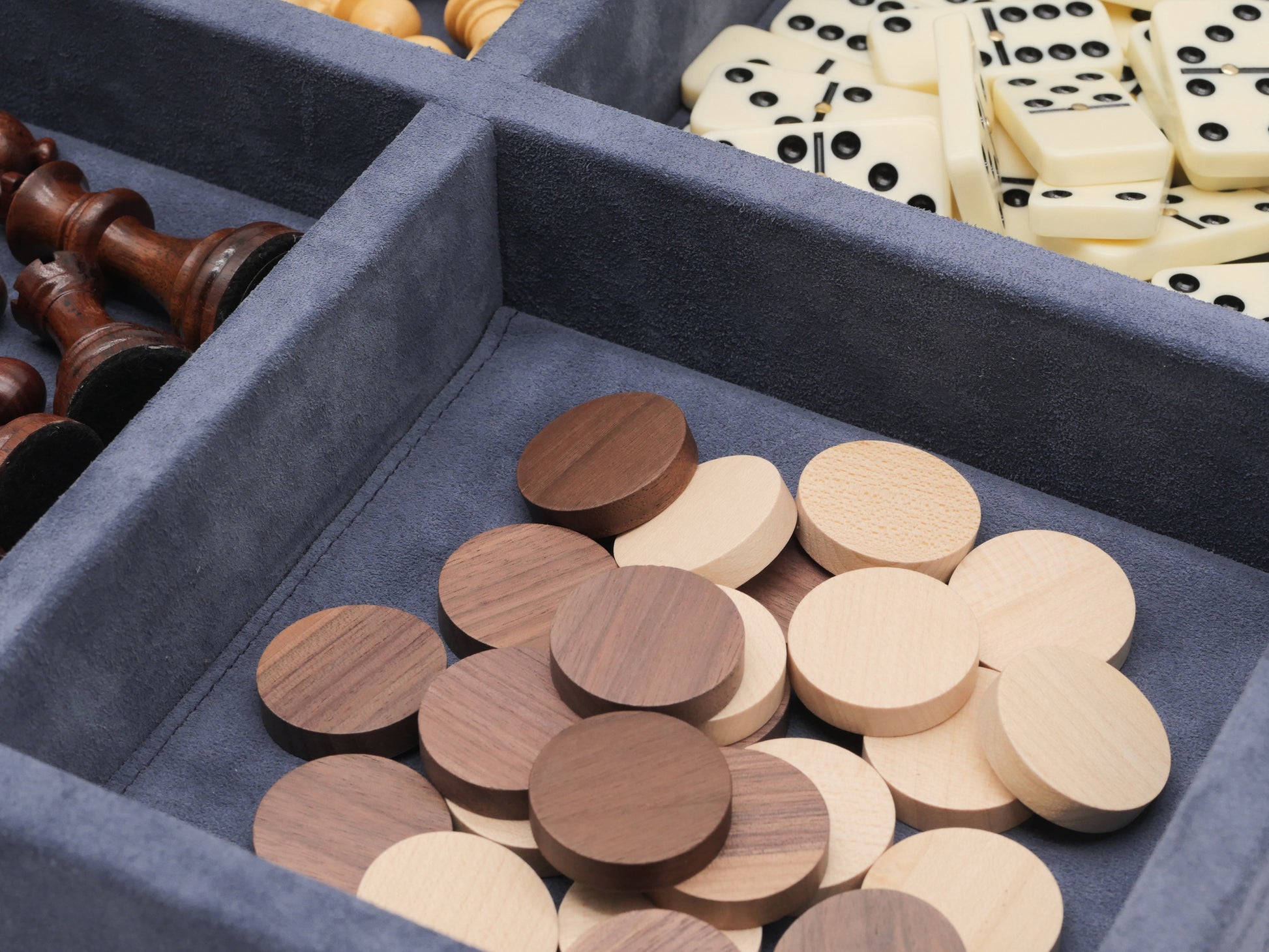 Blue suede case open with wooden chess pieces on the left and cream domino tiles filling the right compartment.