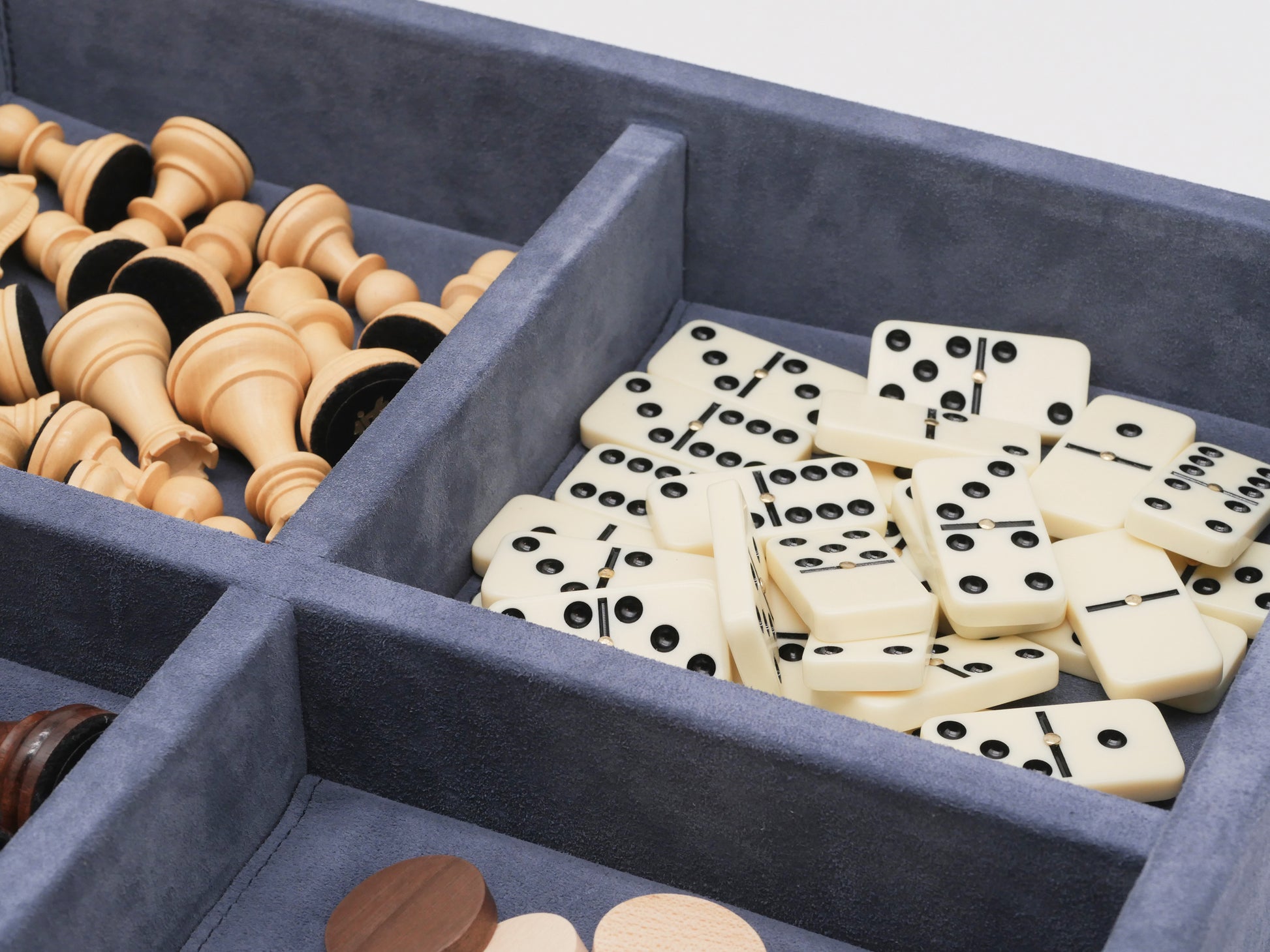 Open blue suede case reveals boxwood chess and checkers pieces on the left and cream dominoes on the right.