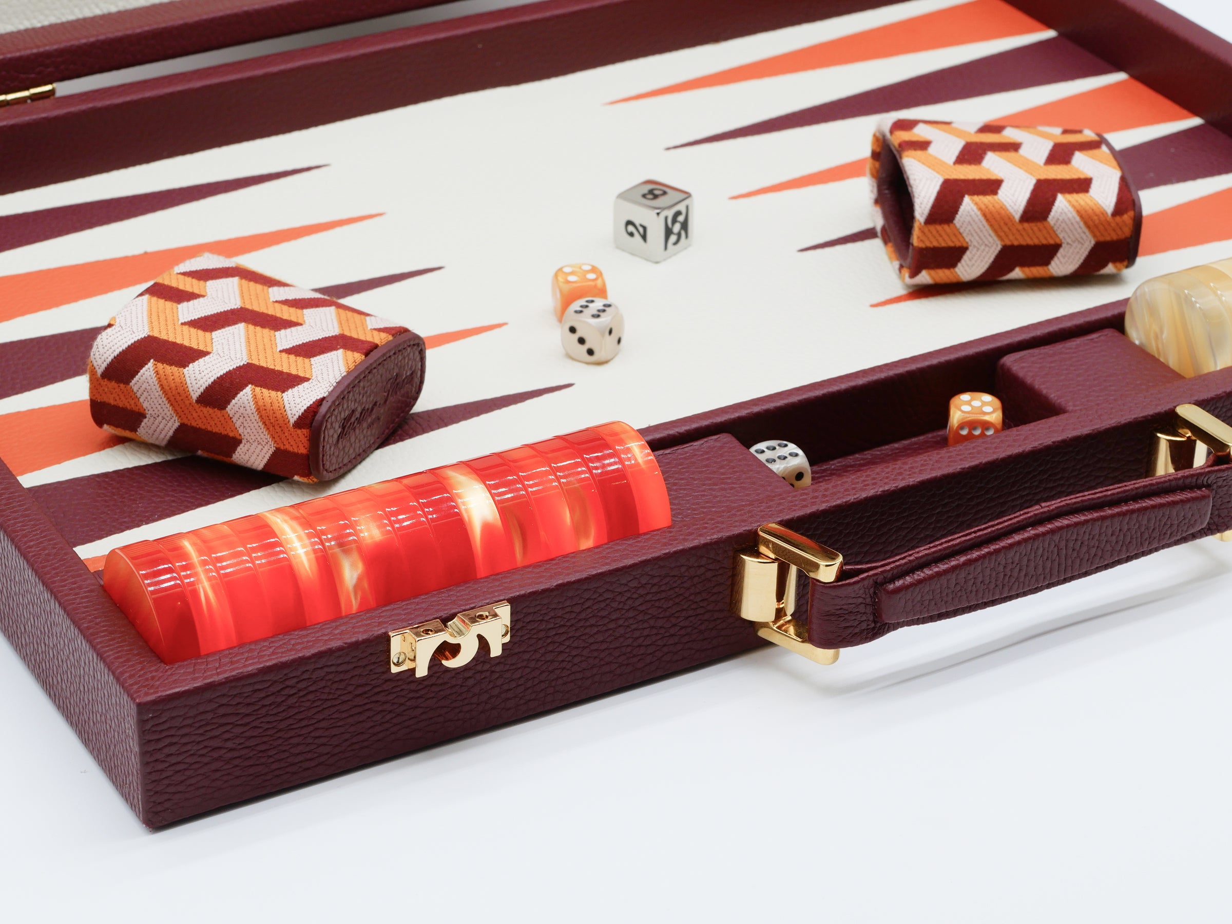 Opened burgundy backgammon case with orange patterned leather dice cups, a red dice tower, and scattered dice on the board