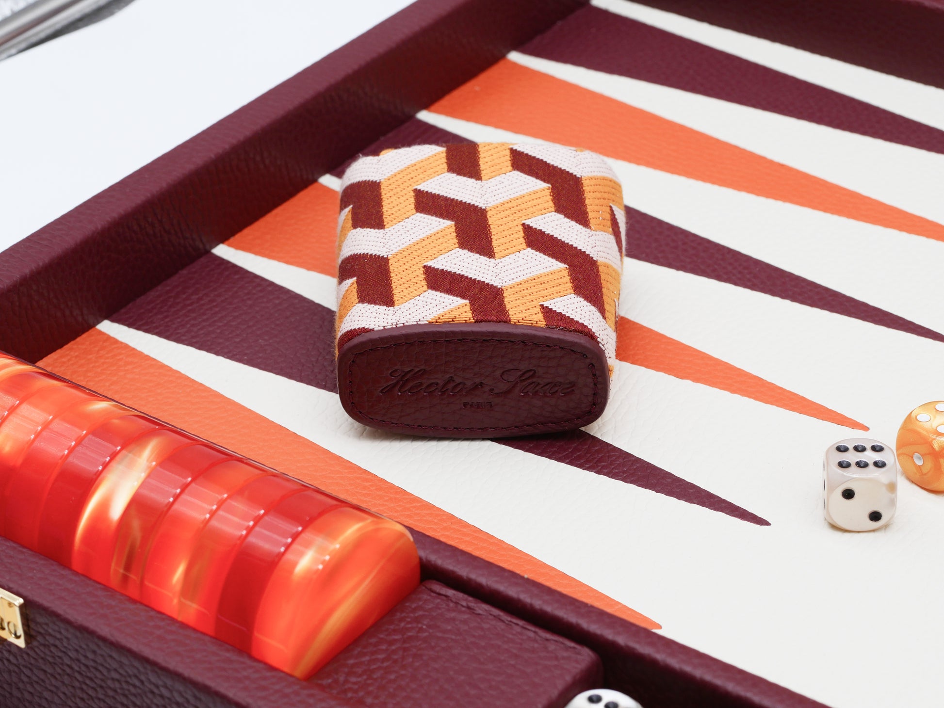 Leather dice cup with orange geometric fabric pattern on burgundy backgammon board