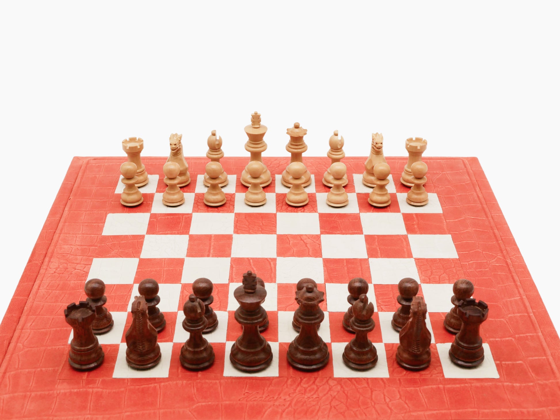 Overhead view of coral leather chessboard with light beige and dark brown chessmen arranged on the playing surface.
