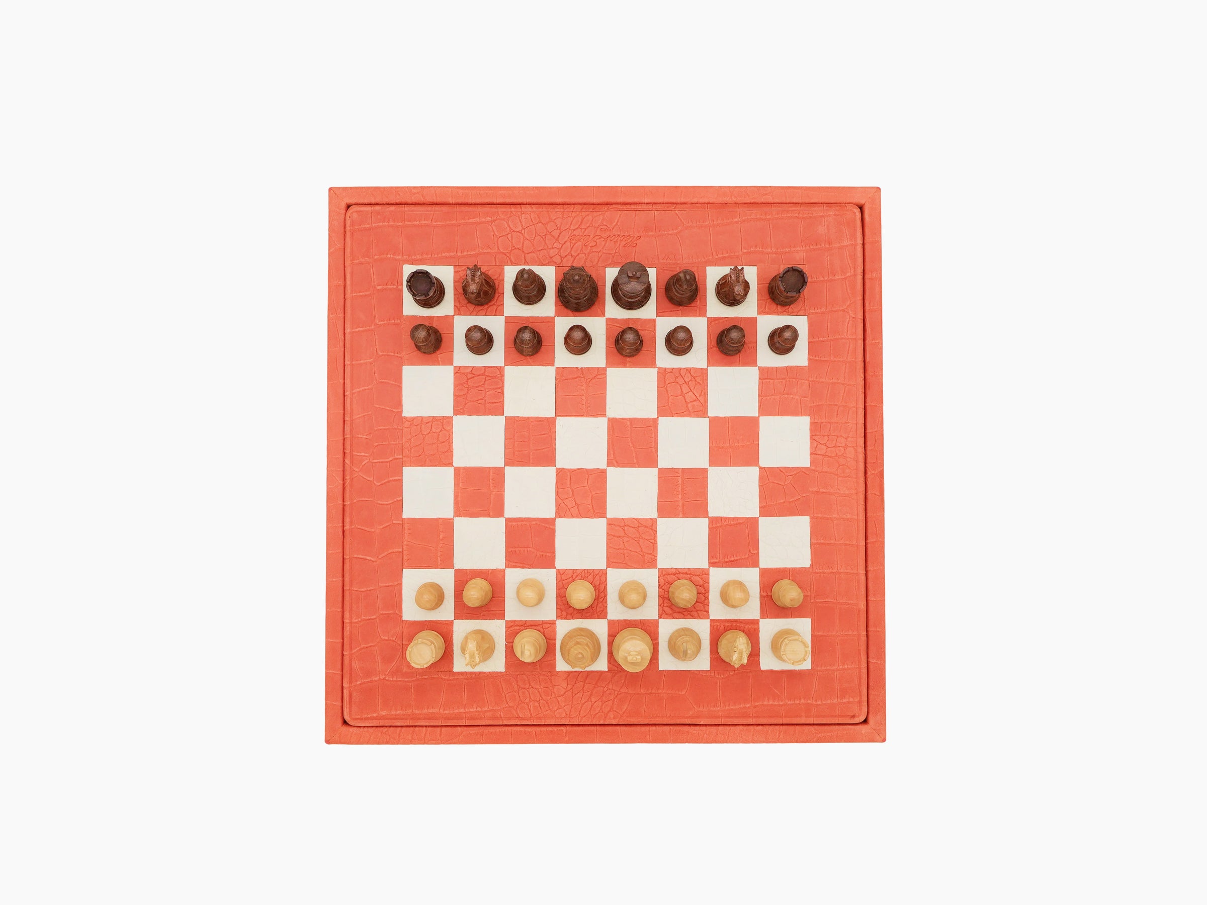Overhead view of coral leather chessboard with light wood and dark pieces in starting position.