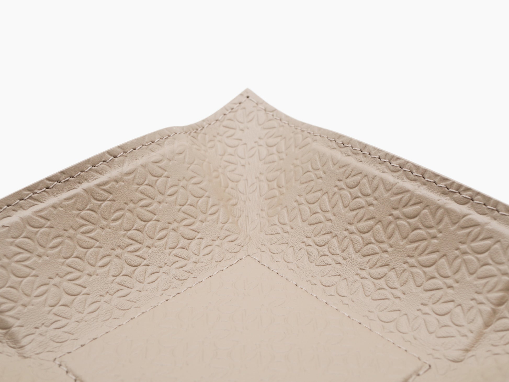 Close up of beige embossed leather showing a repeating monogram pattern and edge stitching