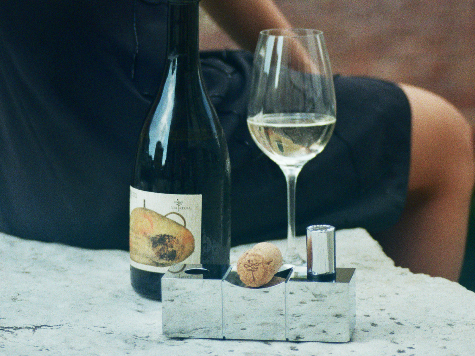 Silver aluminum cork display centerpiece with corks beside a wine bottle and glass.