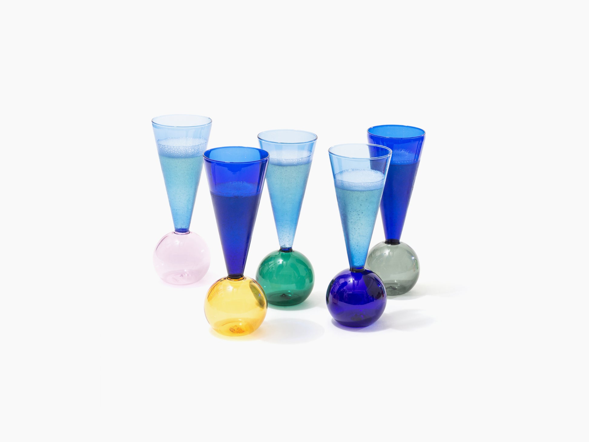 Colorful glass champagne flutes with rounded bases arranged on a white surface