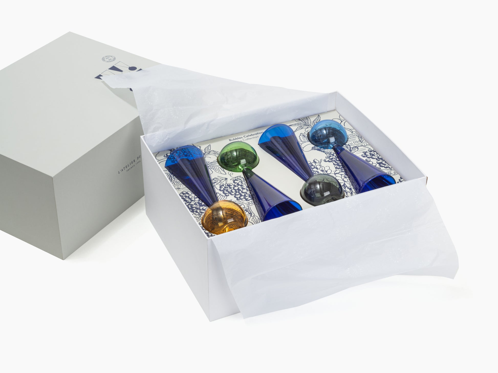 Open packaging for Bubbles Celebration glassware showing blue cobalt flutes nestled in a white box with tissue and a patterned insert