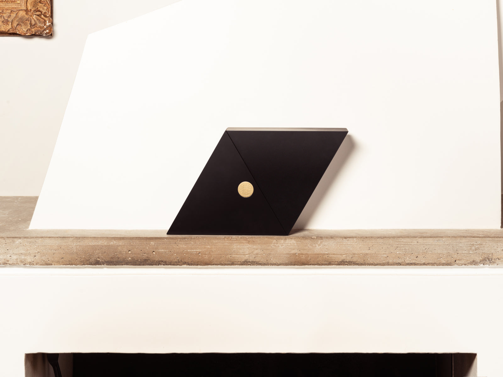Black angular Geometry box with a gold medallion on the front sits on a white shelf