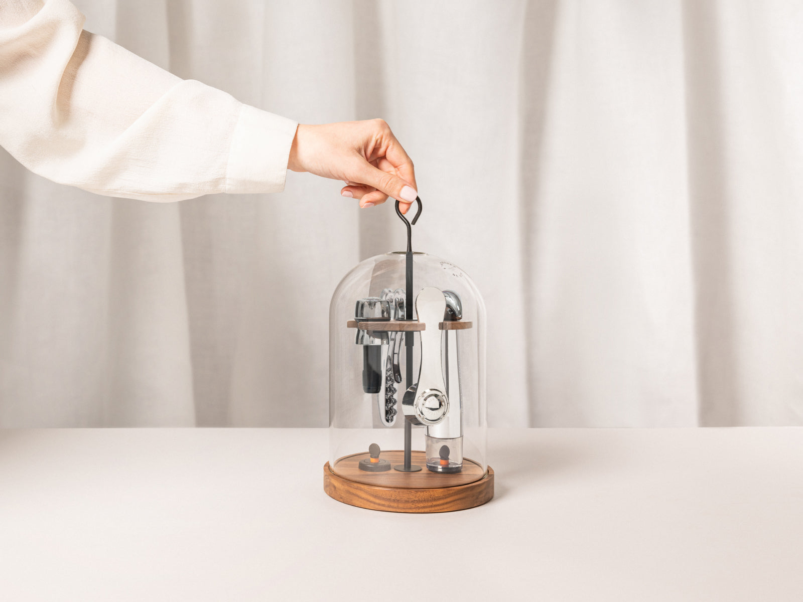 Hand lifting Le Globe wine tasting set under a glass dome on a walnut base with cork opener and accessories visible