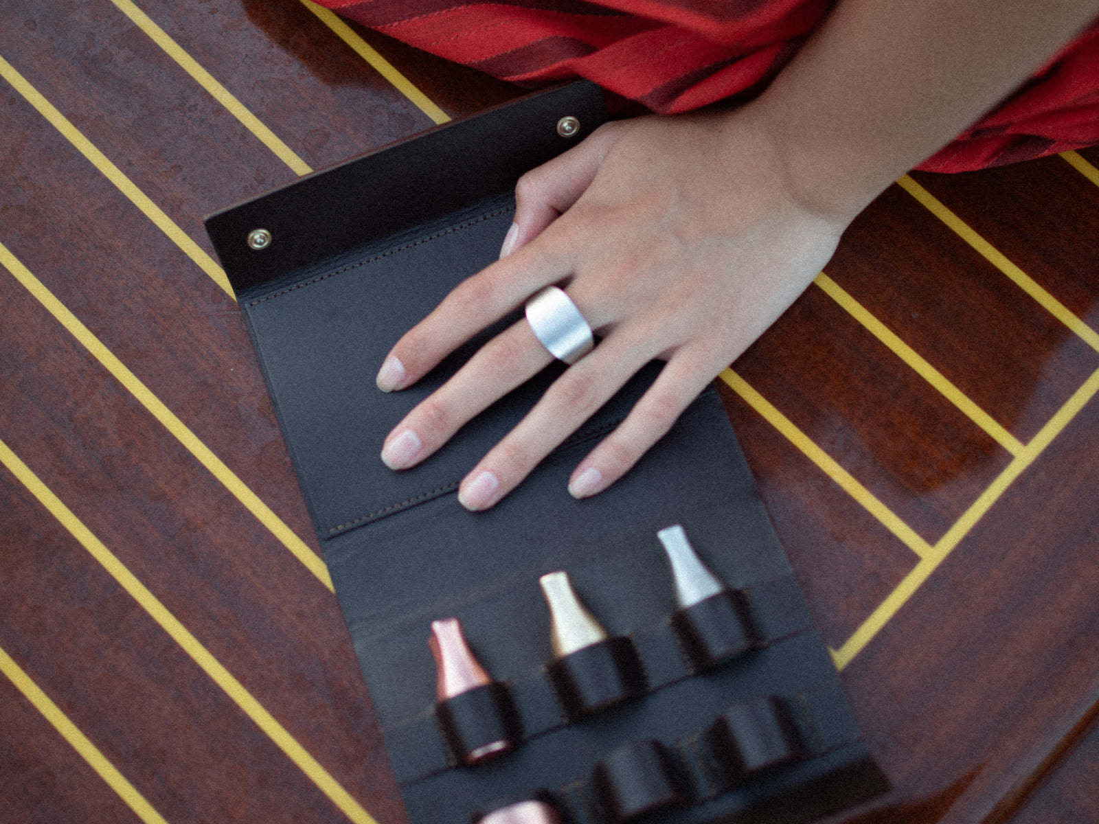 Open black leather case displaying six metal wine stoppers; a hand with a bold silver ring rests nearby.