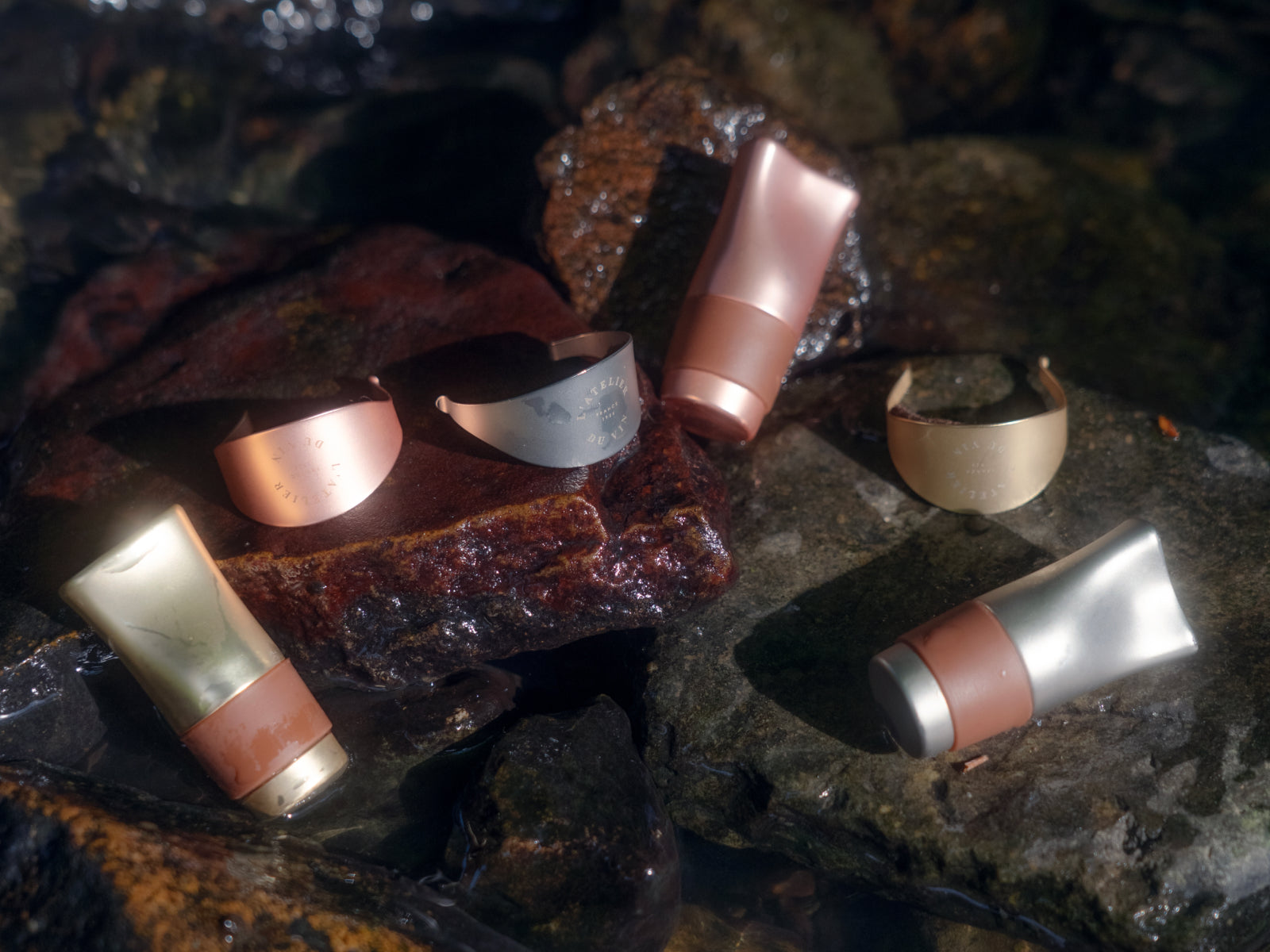 Six matte metal wine accessories including stoppers and rings scattered on a rocky surface.