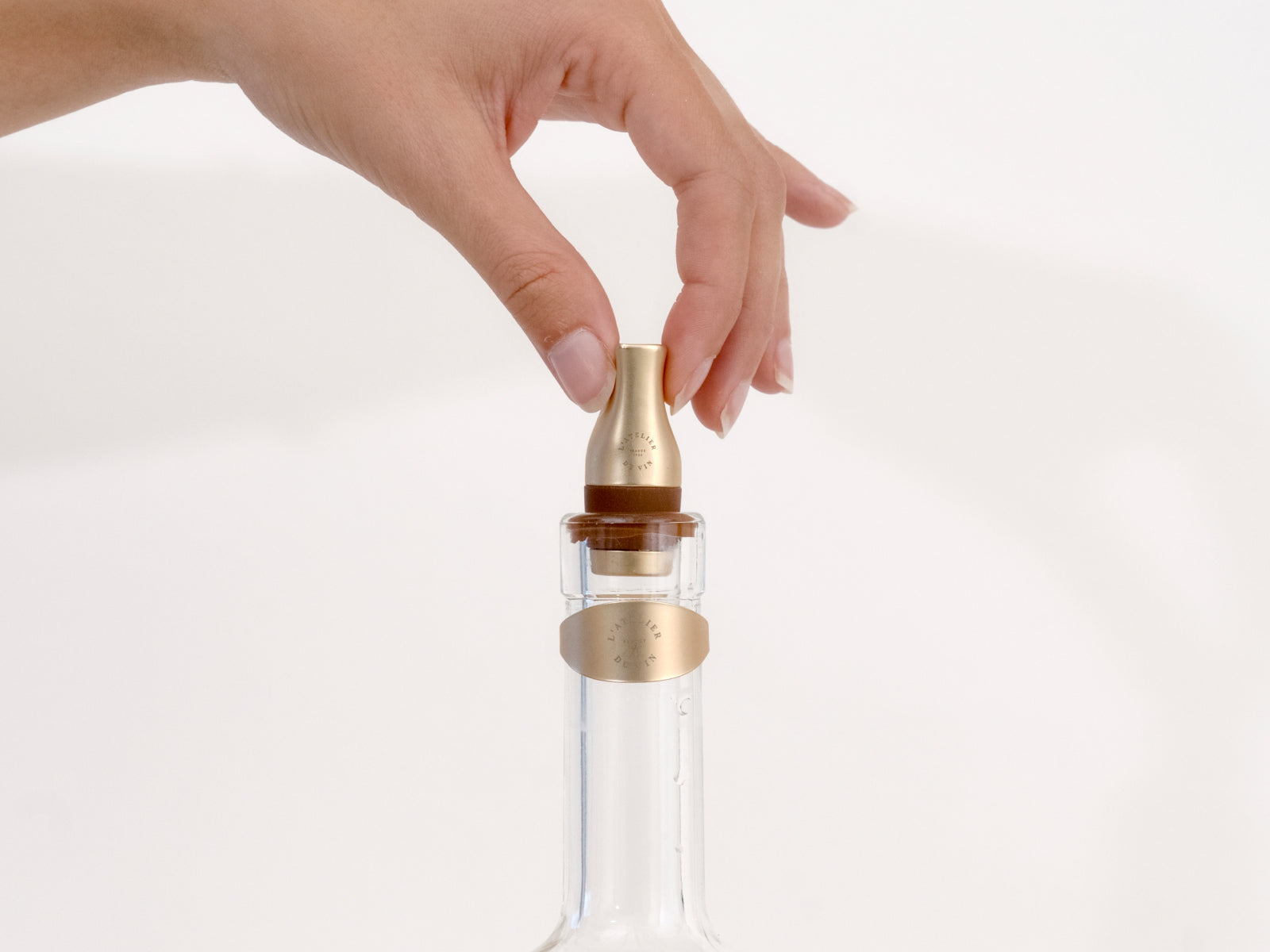 Hand places a gold toned wine stopper into a clear glass bottle.