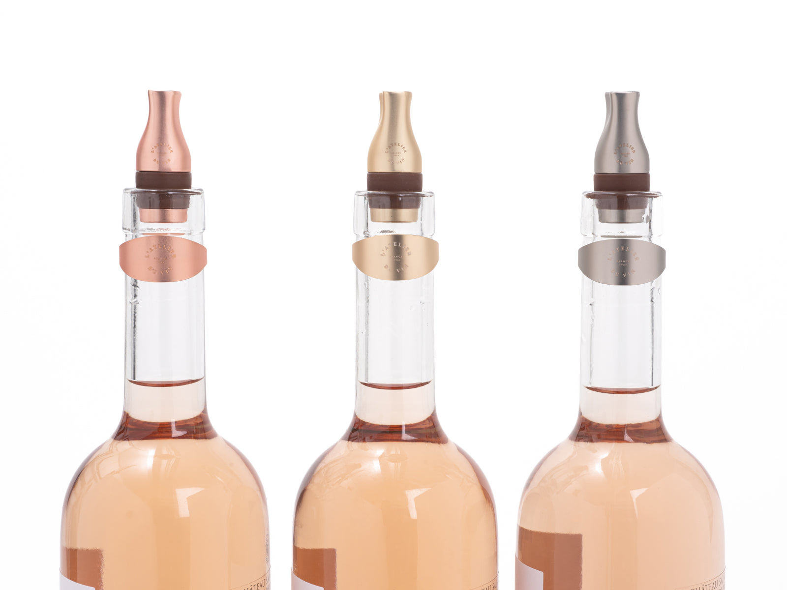 Three wine bottles with matching stoppers in rose gold, gold, and silver.