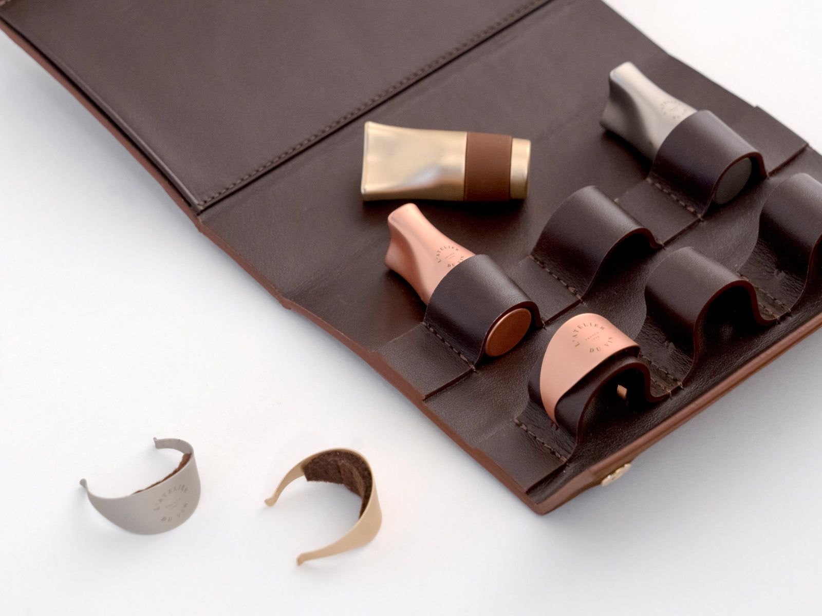 Opened brown leather case displaying three stoppers and three rings tucked into leather loops.
