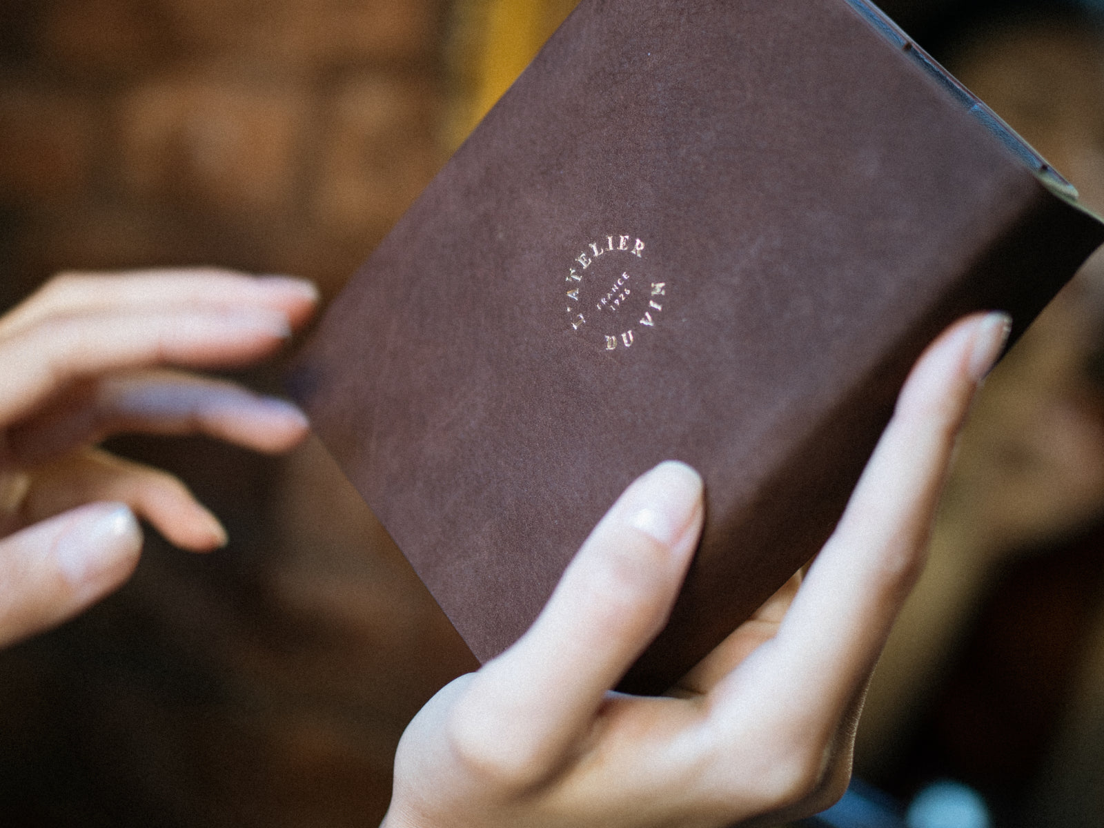 Hands hold a brown leather Les Bijoux wine accessories case with a circular gold logo.