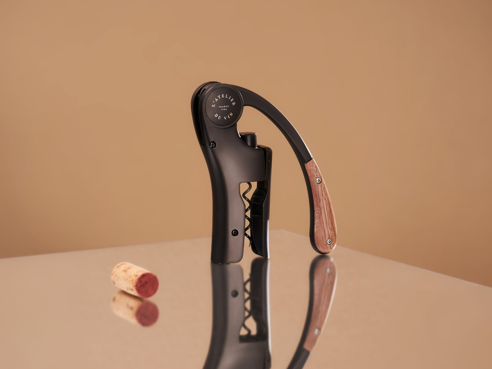 Oeno Motion corkscrew with wood and black handle on a reflective surface beside a cork