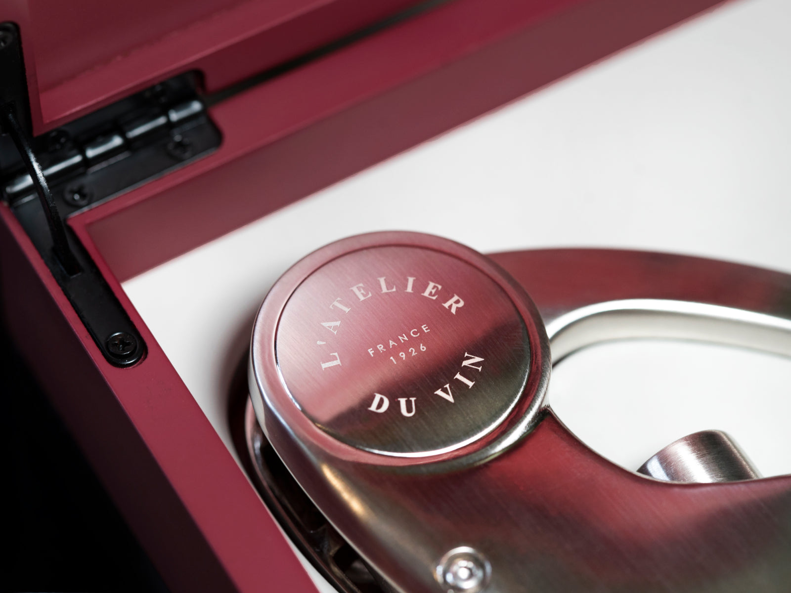 Open red lacquered case displaying a polished stainless corkscrew with a white interior and the L Atelier du Vin stamp.