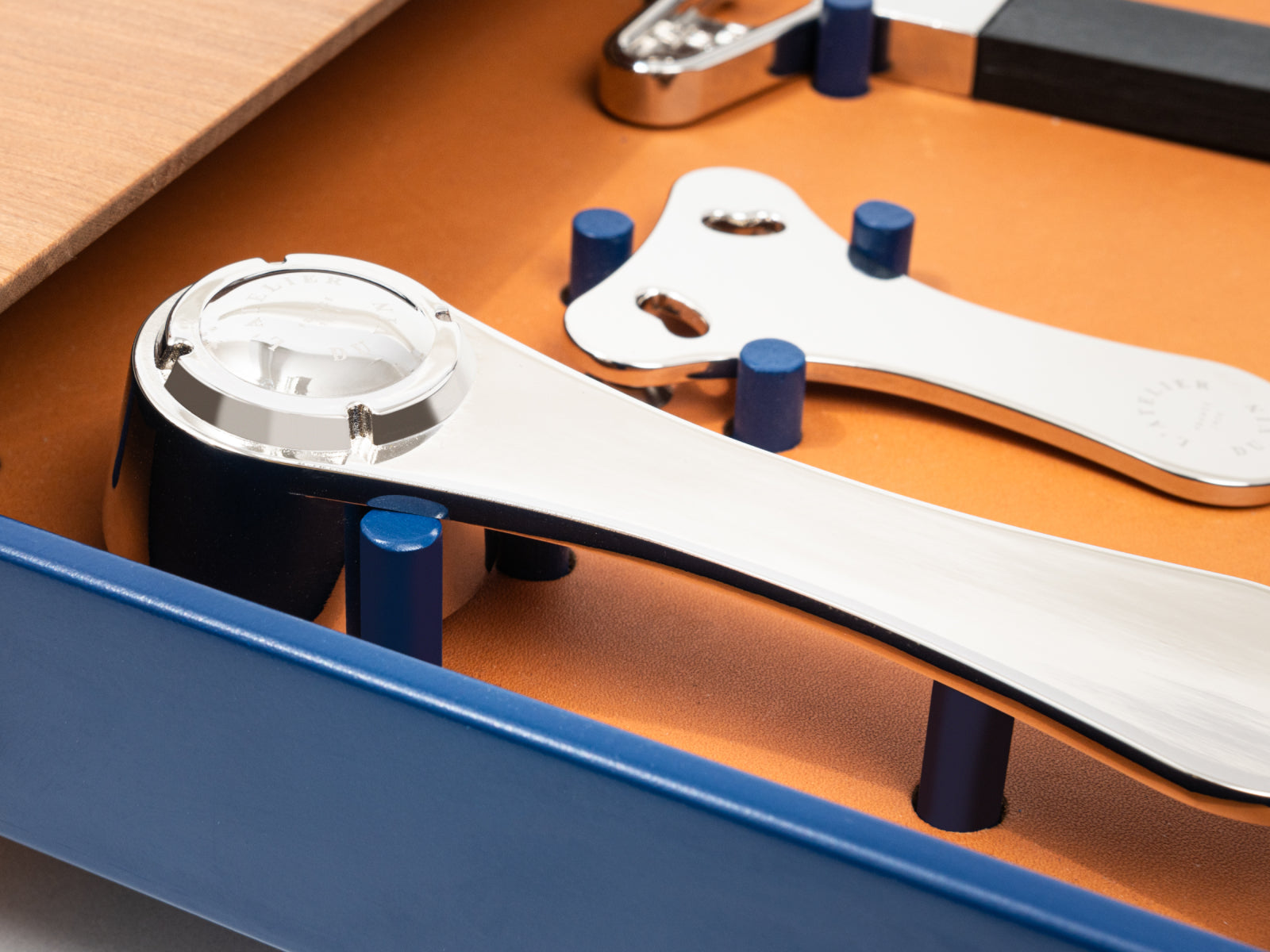 Close-up of Le Plateau assembly with a curved silver mechanism and white panel on an orange base with blue pegs
